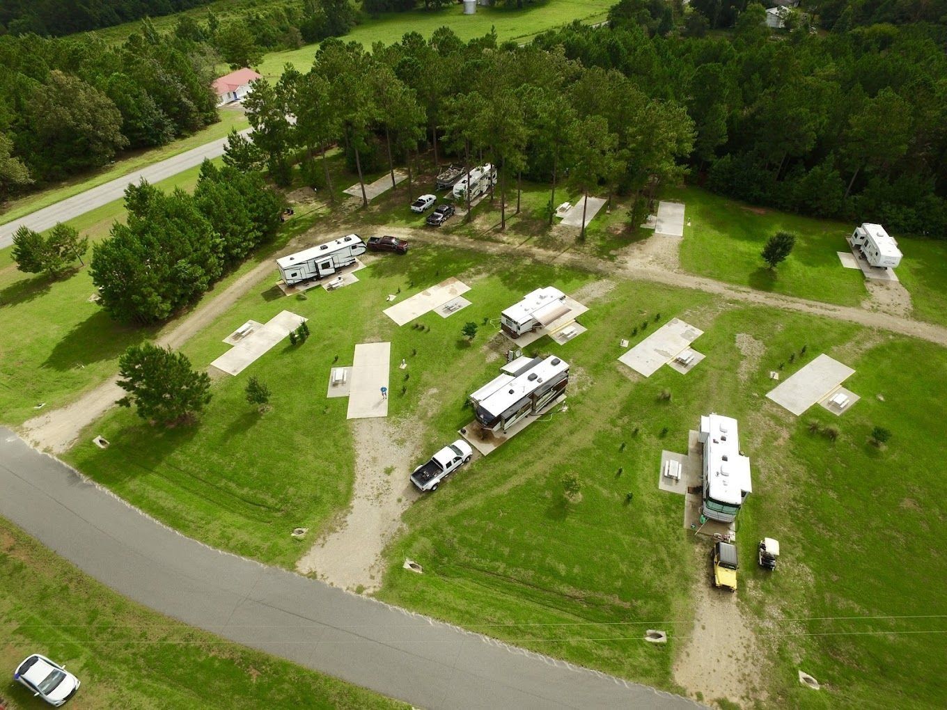 Aerial view of an RV park with several RVs parked on grass plots, surrounded by trees and a paved road.