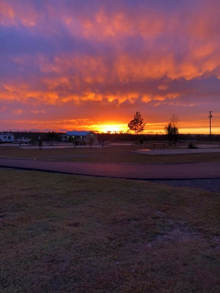Sunset over a golf course with vibrant orange and purple clouds; horizon and buildings in silhouette.