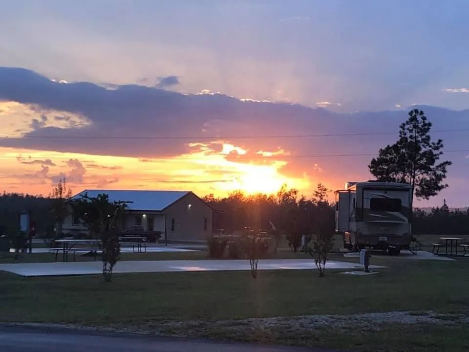 Sunset over RV park with sun rays, RVs, and small building, and lush green grass.