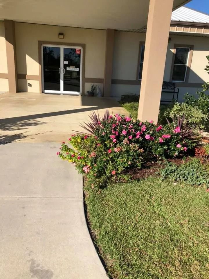 Entrance with glass doors, sidewalk, and landscaped garden with pink flowers.