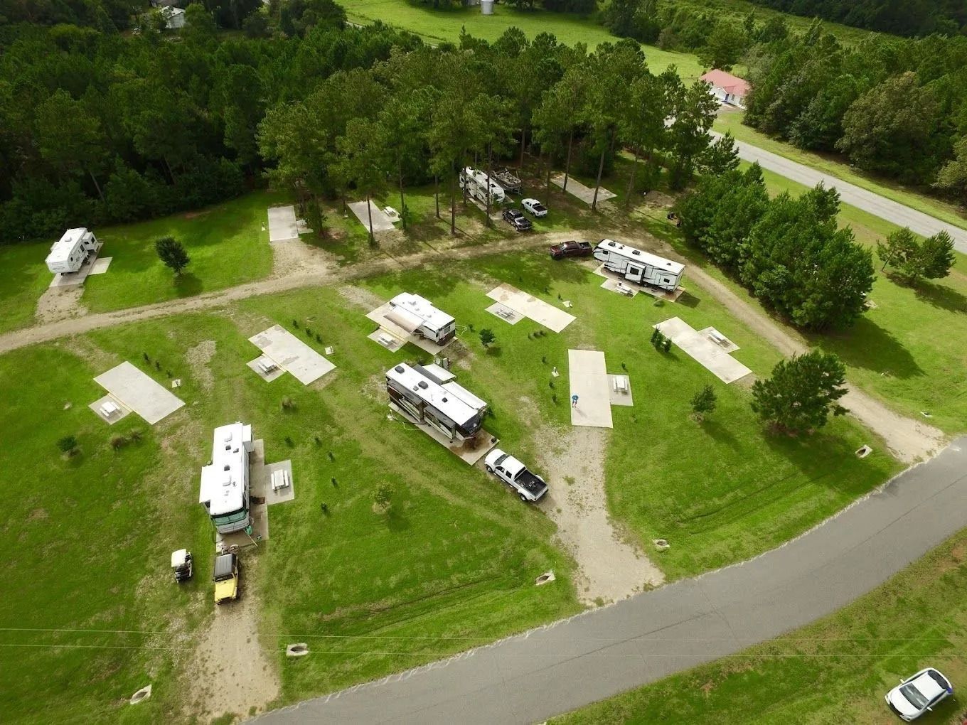 Aerial view of an RV park with multiple RVs parked on grassy lots with concrete pads.
