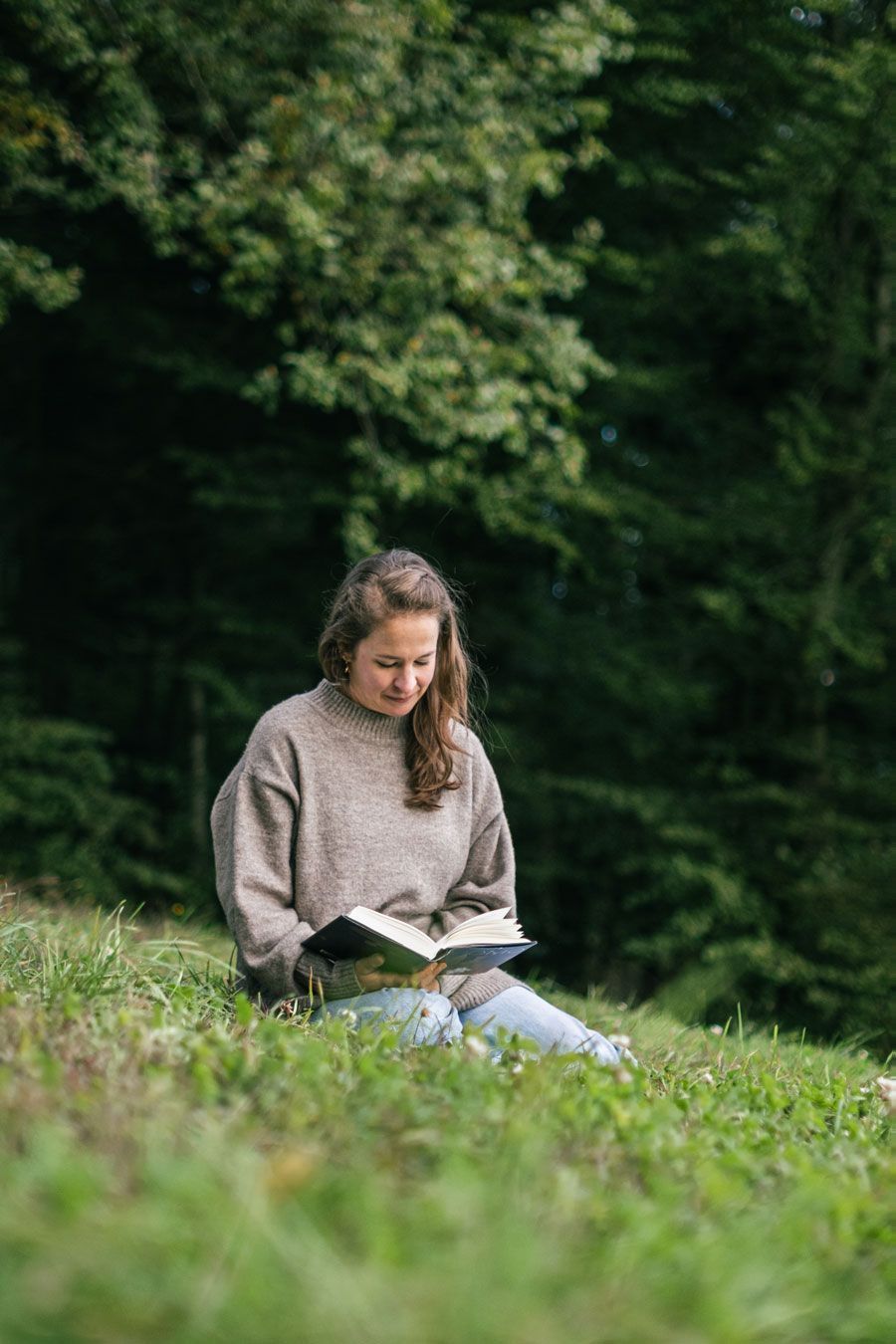 Eine Frau sitzt unter einem Baum und liest ein Buch.