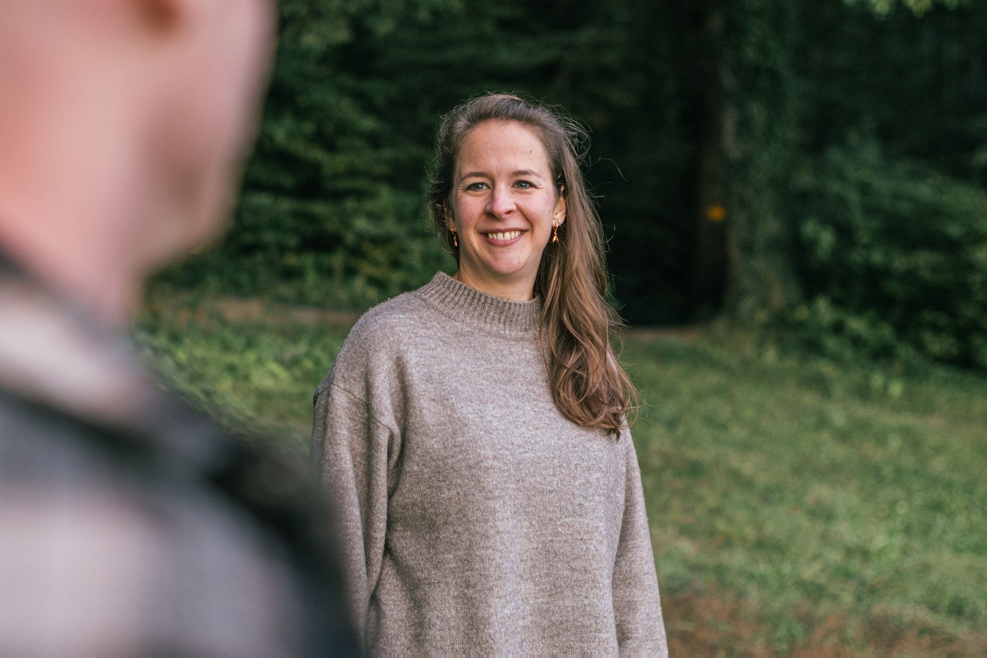 Eine Frau im Freien, lächelnd in die Kamera, vor grünem Hintergrund.