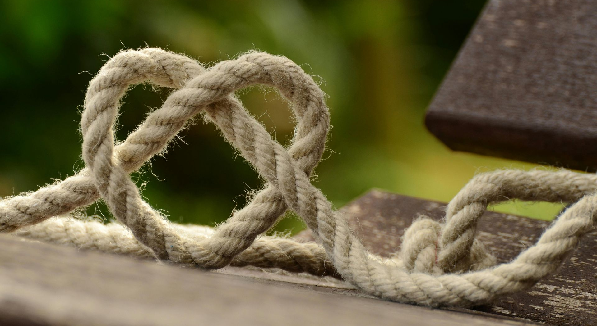 Ein Seil, zu einem Herz gelegt, auf Holz vor grünem Hintergrund – Symbol für Verbindung und Nähe.
