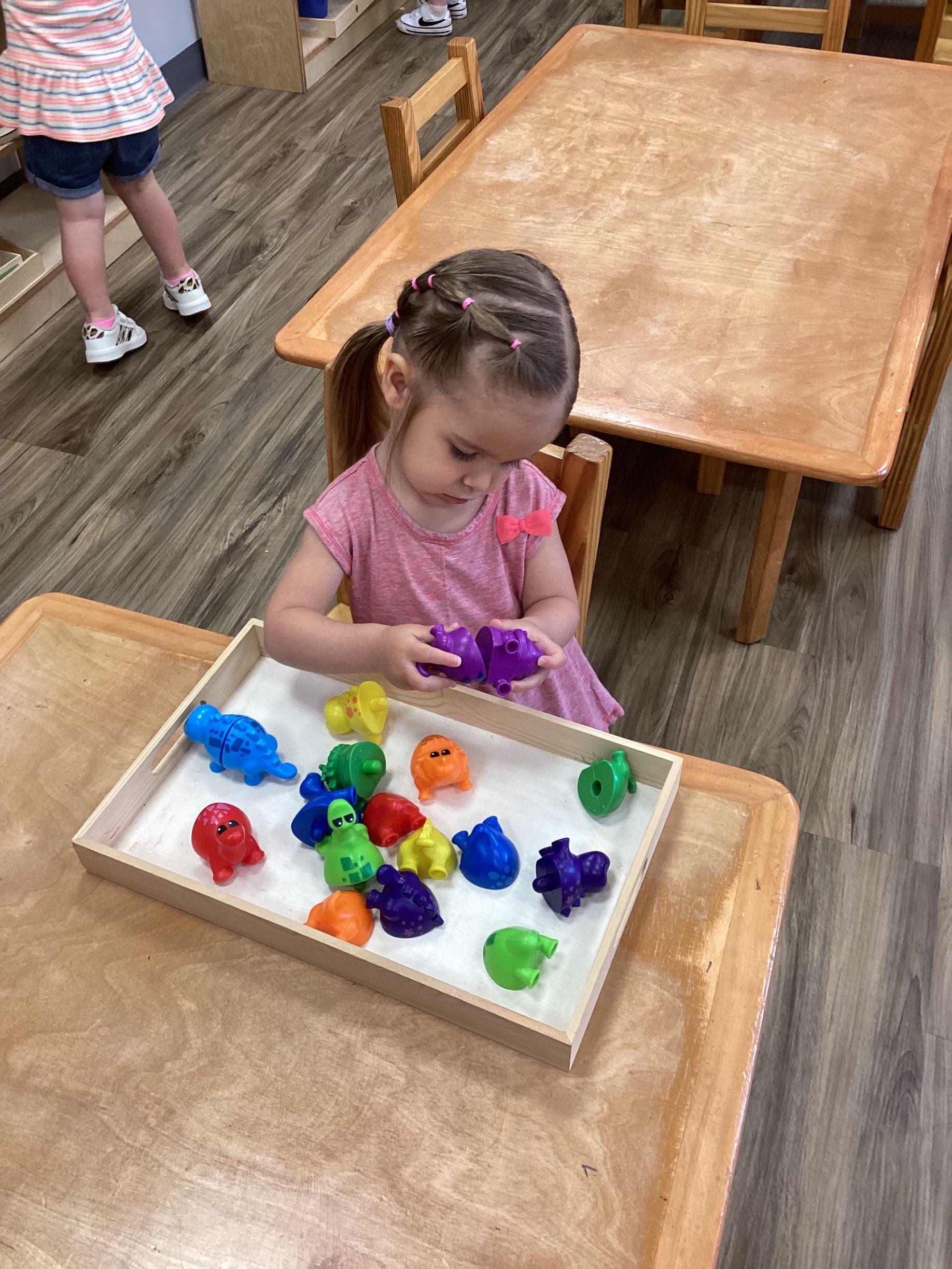 Child playing with colorful toy animals at a table in a classroom
