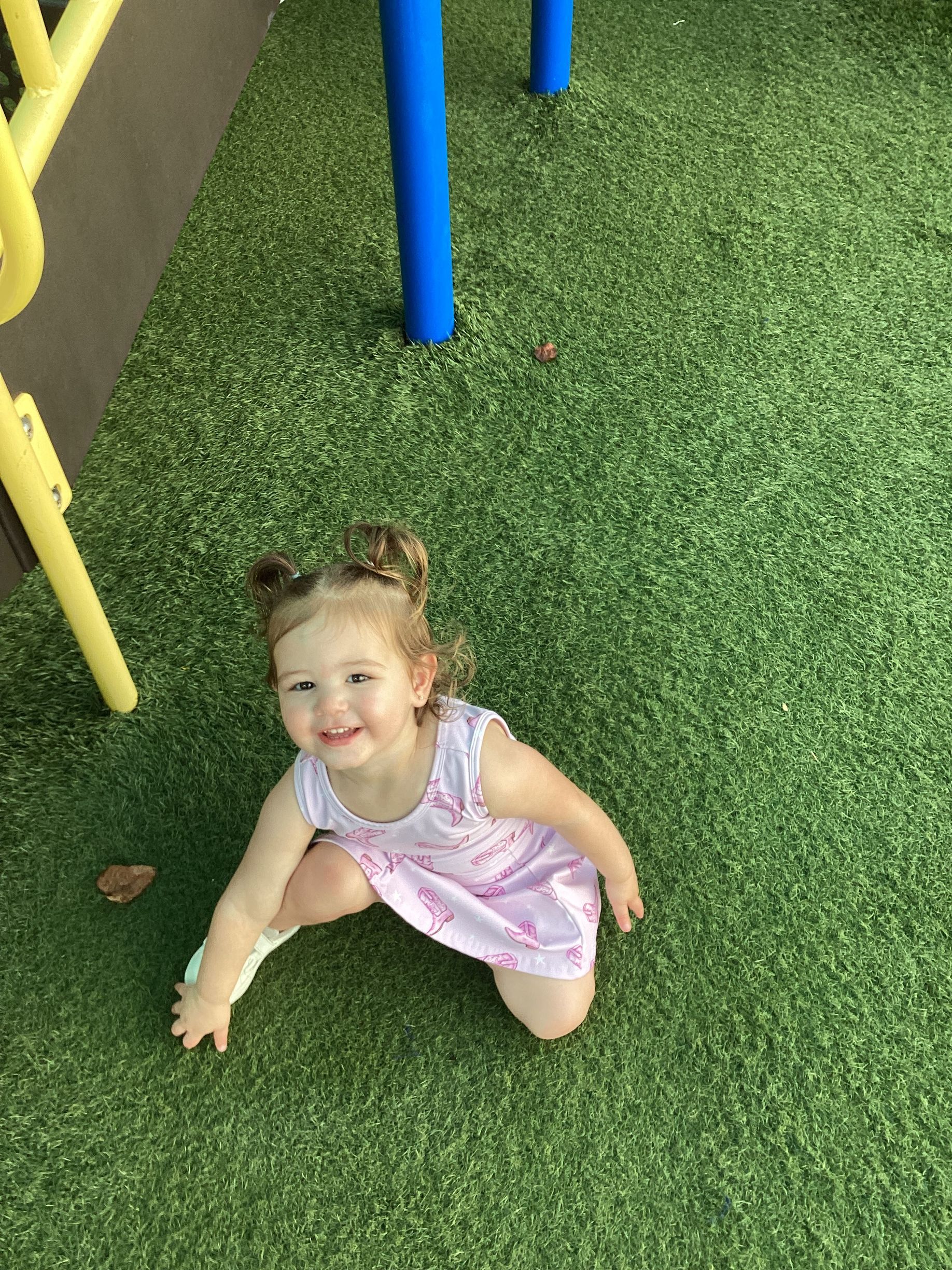 Smiling child kneeling on green turf near blue and yellow playground poles