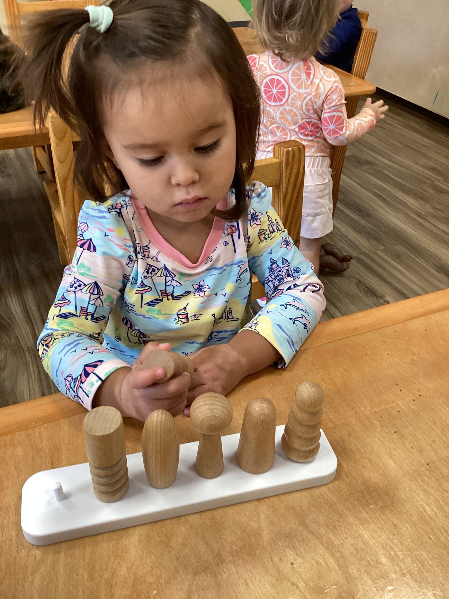 Child playing with a wooden sorting toy at a table in a classroom