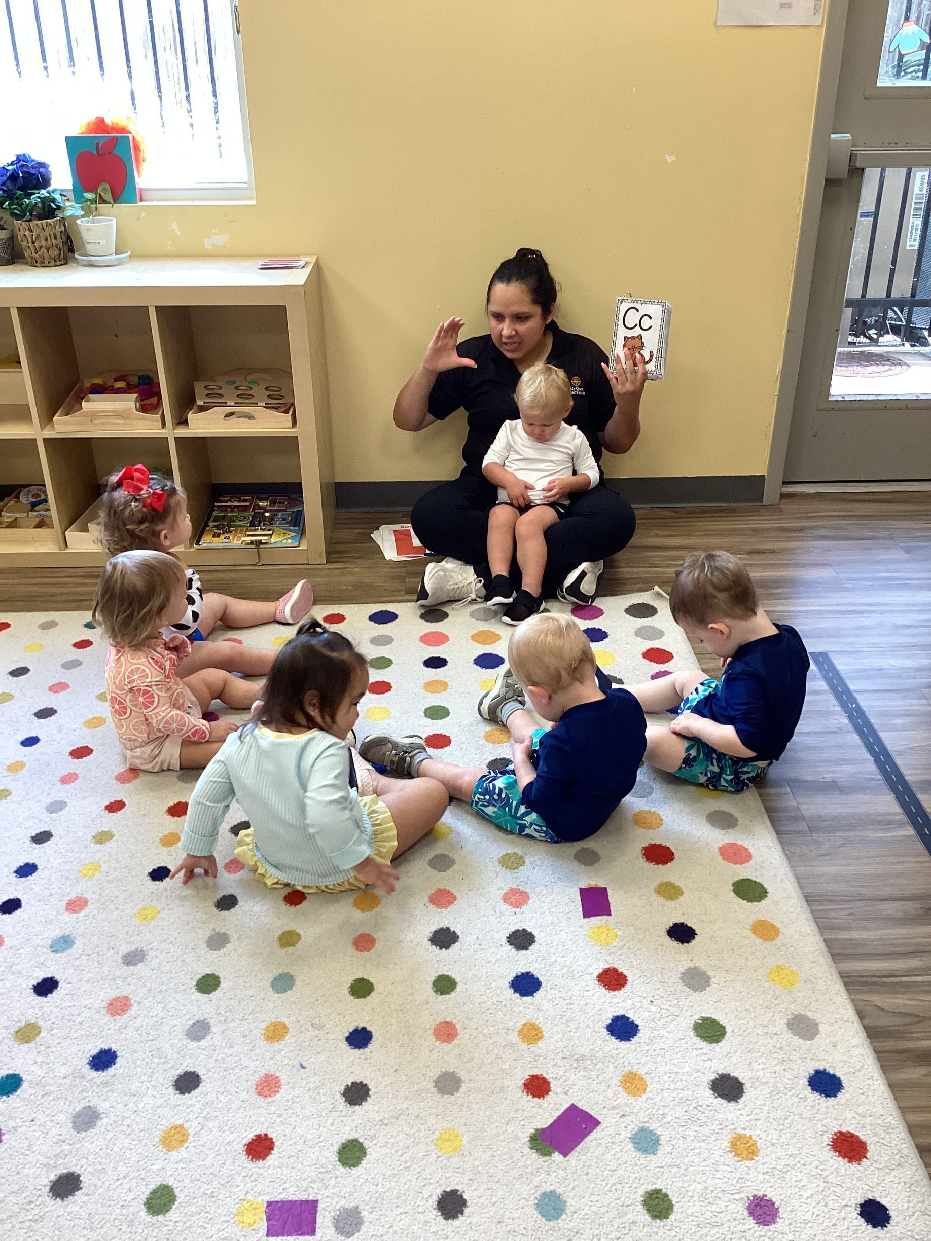 Caregiver sitting with several babies on a colorful polka-dot rug in a playroom