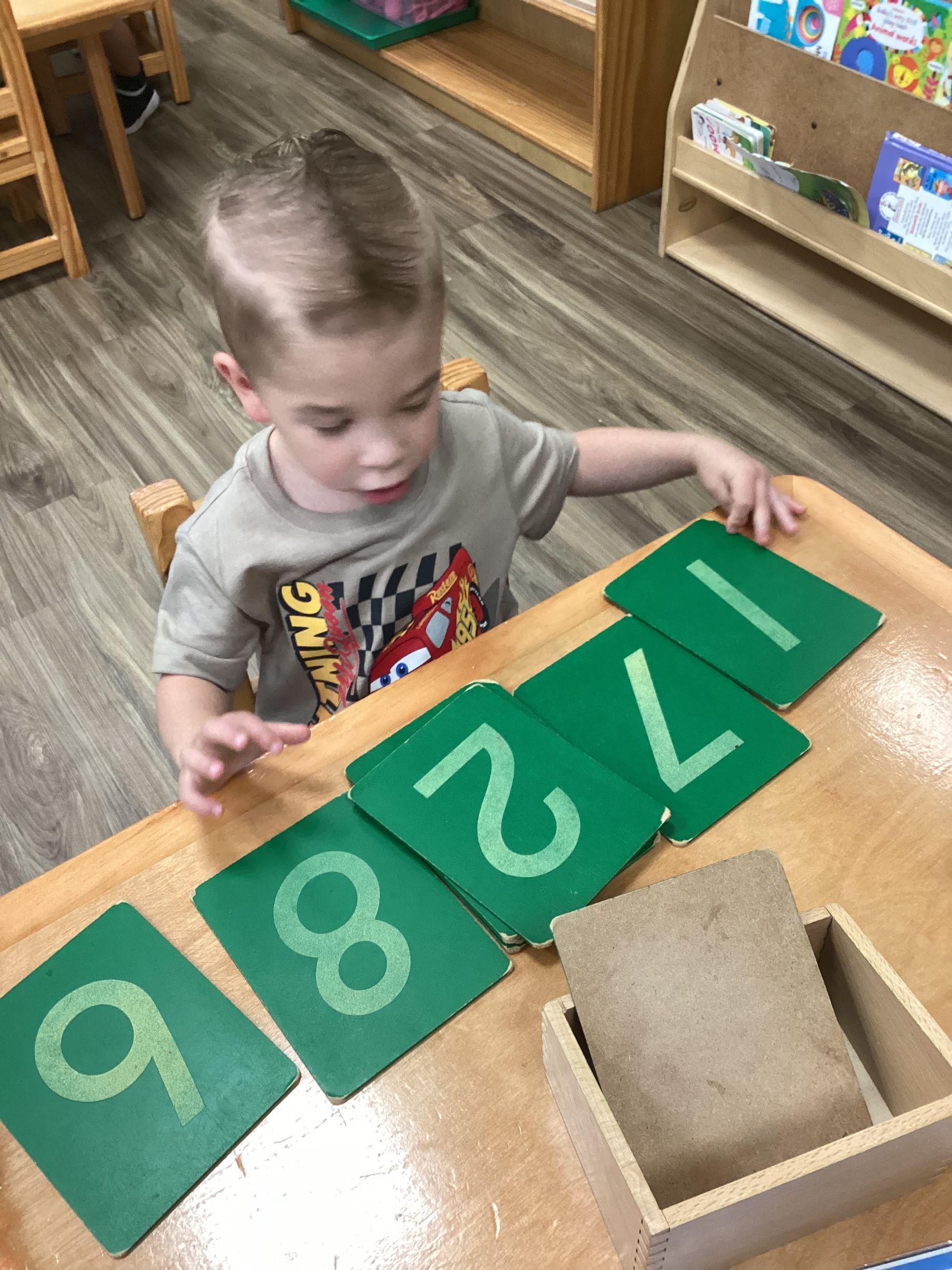 Child counting with green number cards at a classroom table