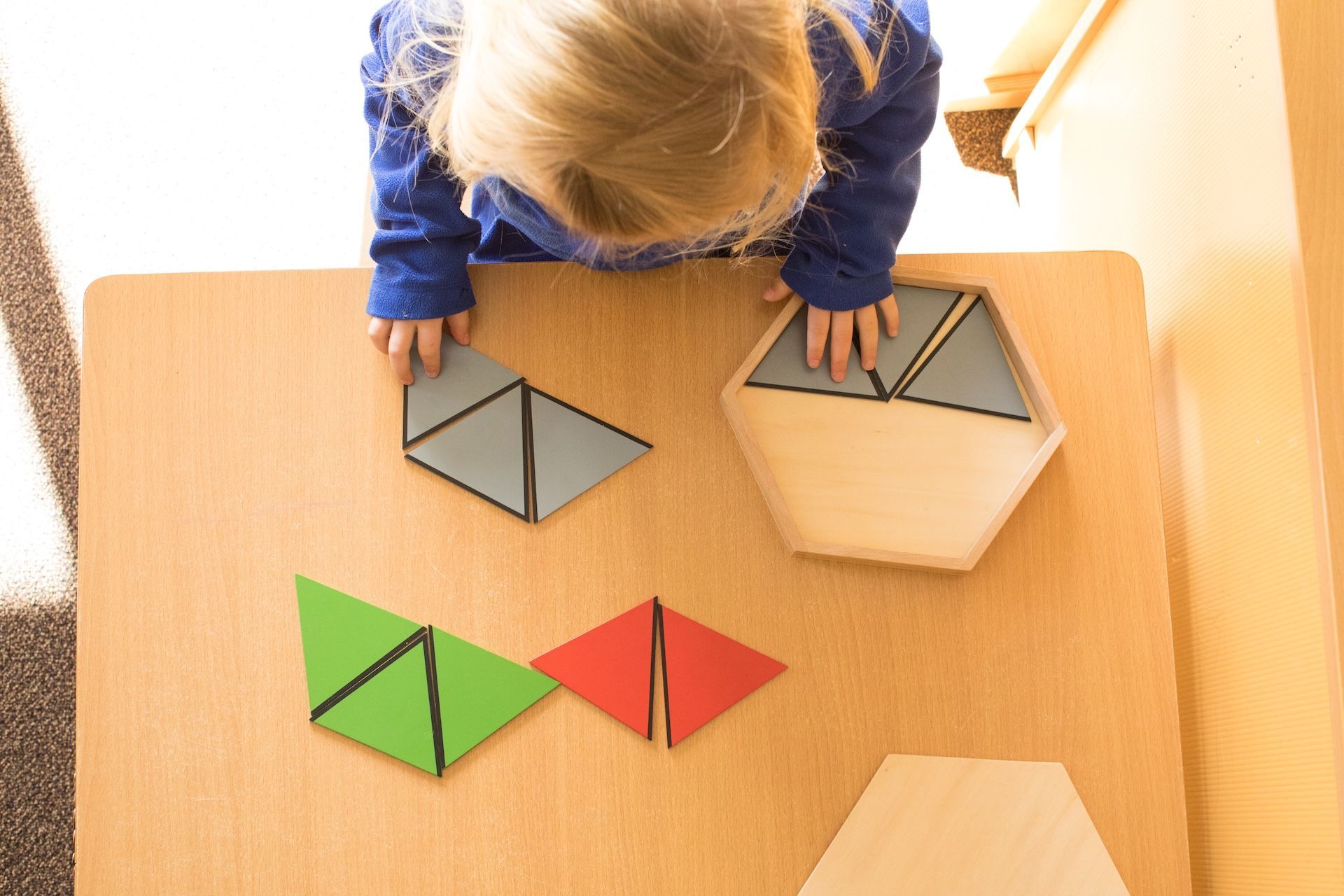 Child arranging colorful geometric shapes on a wooden table