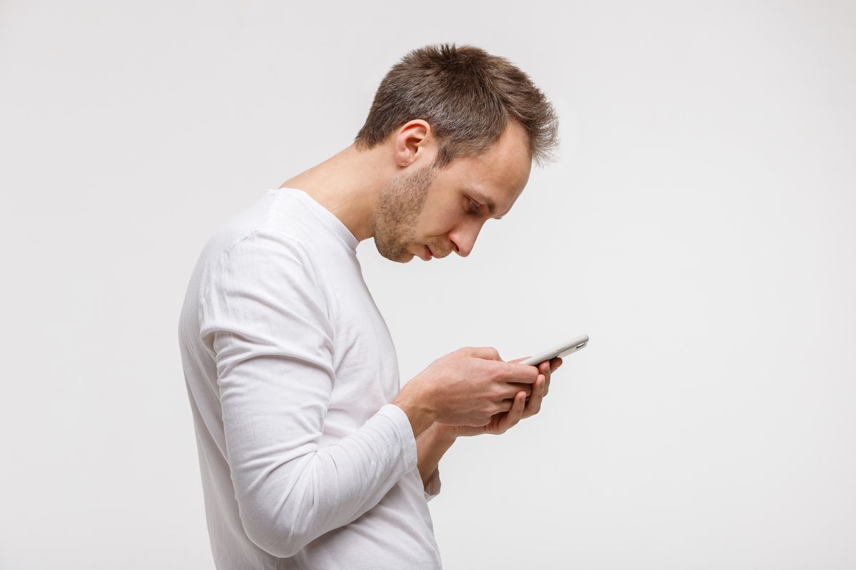 Person in a white shirt looking down at a smartphone against a plain light background