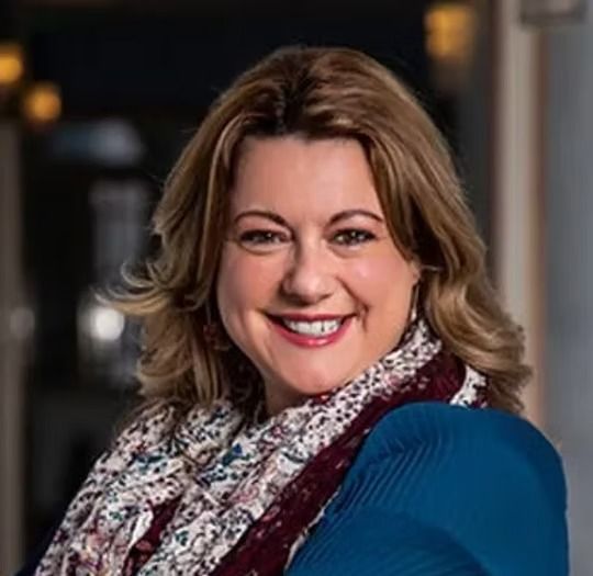 Smiling woman in a blue sweater and patterned scarf, posed indoors against a softly blurred background