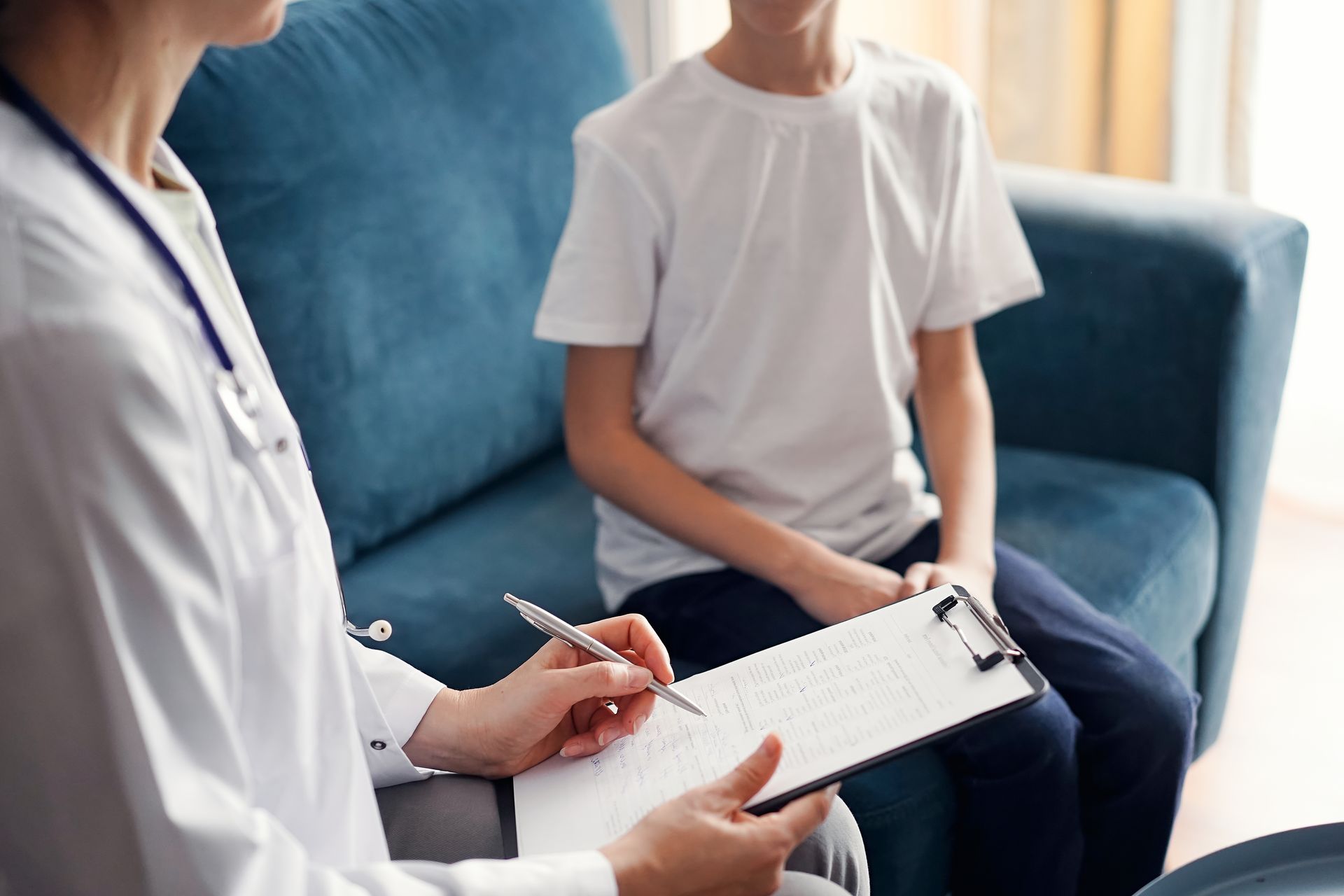 Therapist taking notes while speaking with a seated client in a bright office