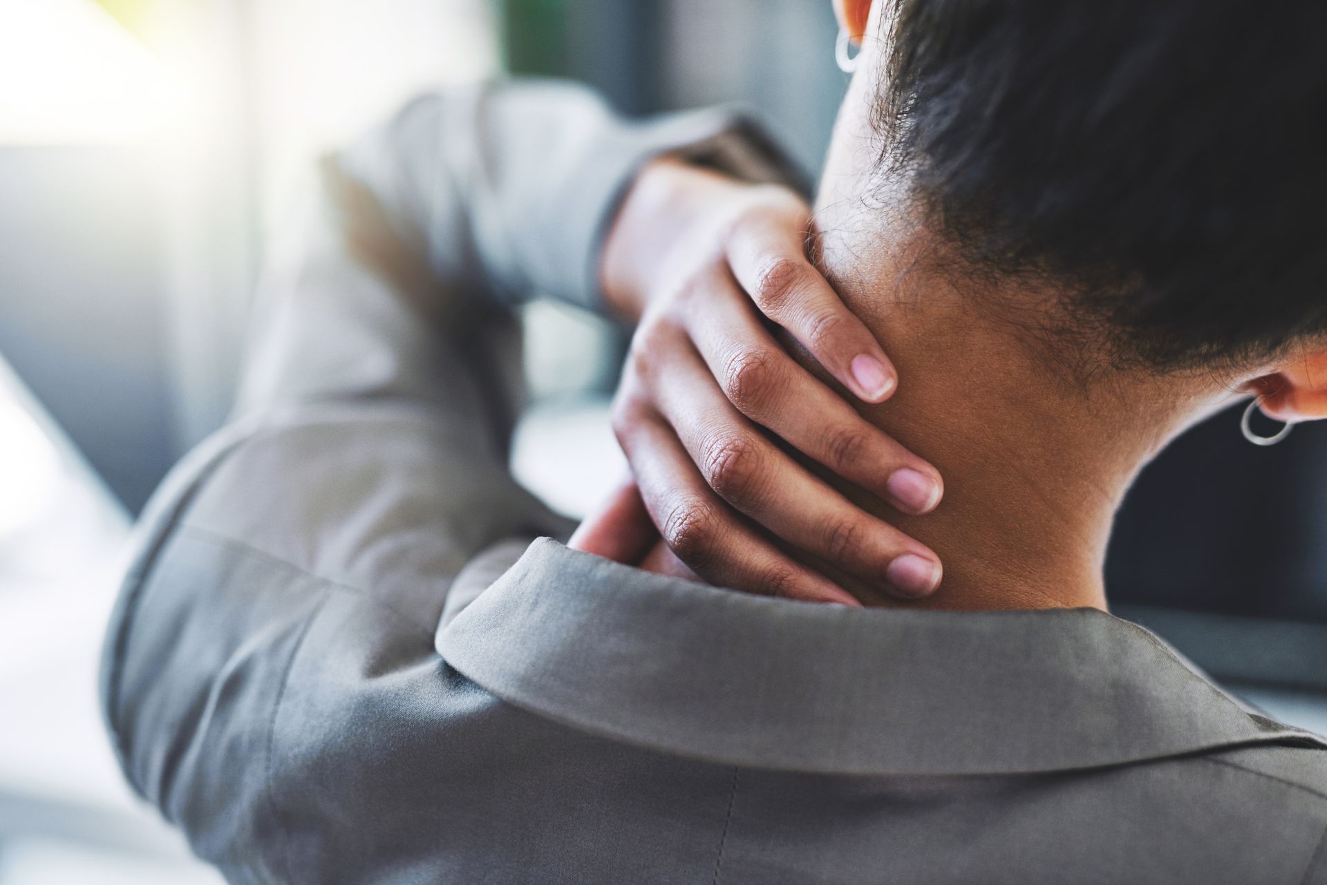 Person holding the back of their neck, suggesting pain or stiffness in the neck.