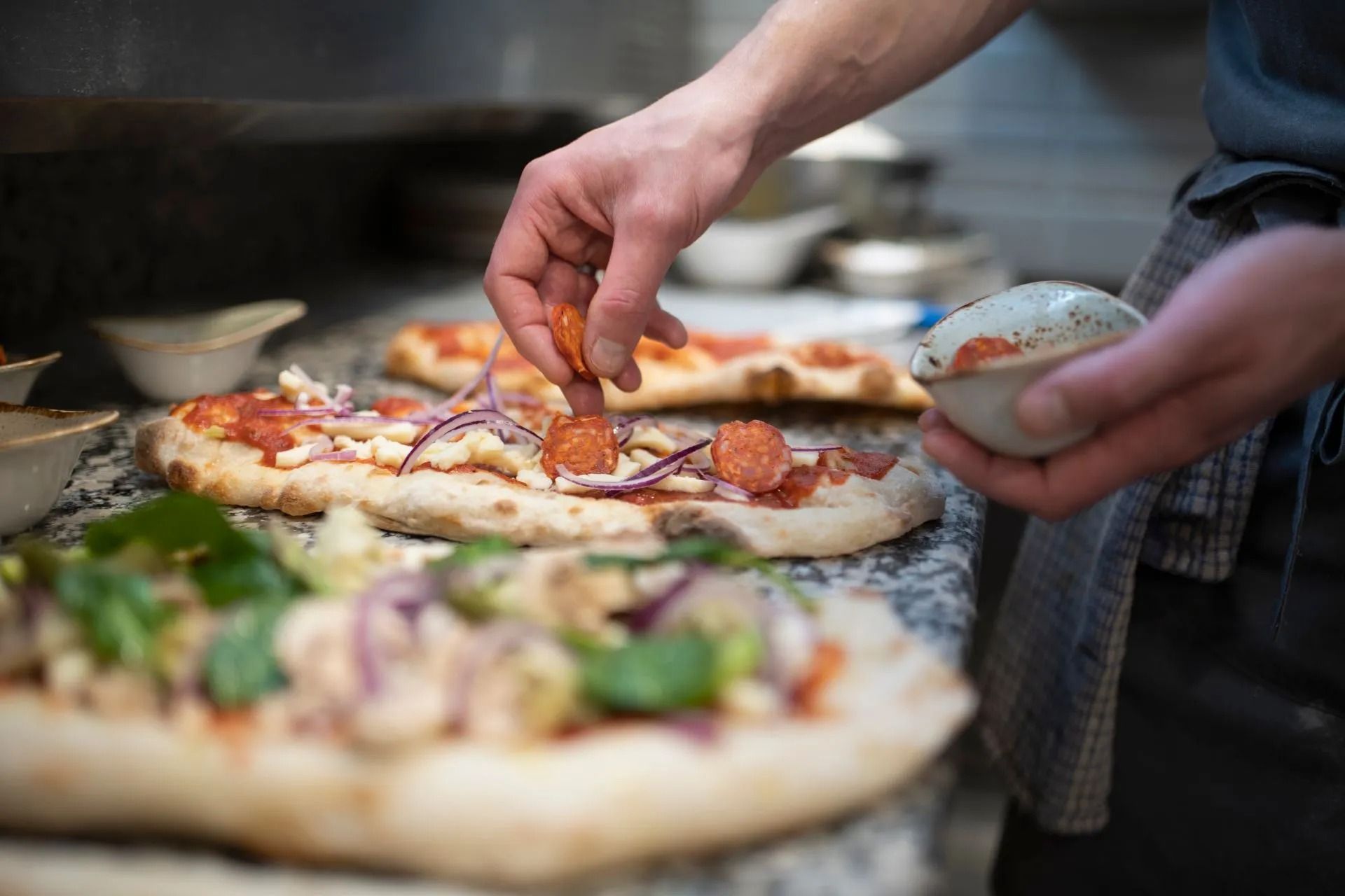 Persona che aggiunge il salame piccante alla pizza in cucina.