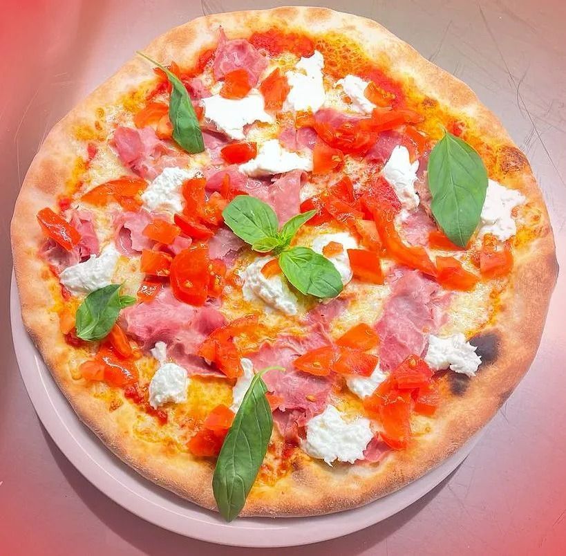 Pizza condita con salsa rossa, prosciutto, pomodori a cubetti, mozzarella e basilico.