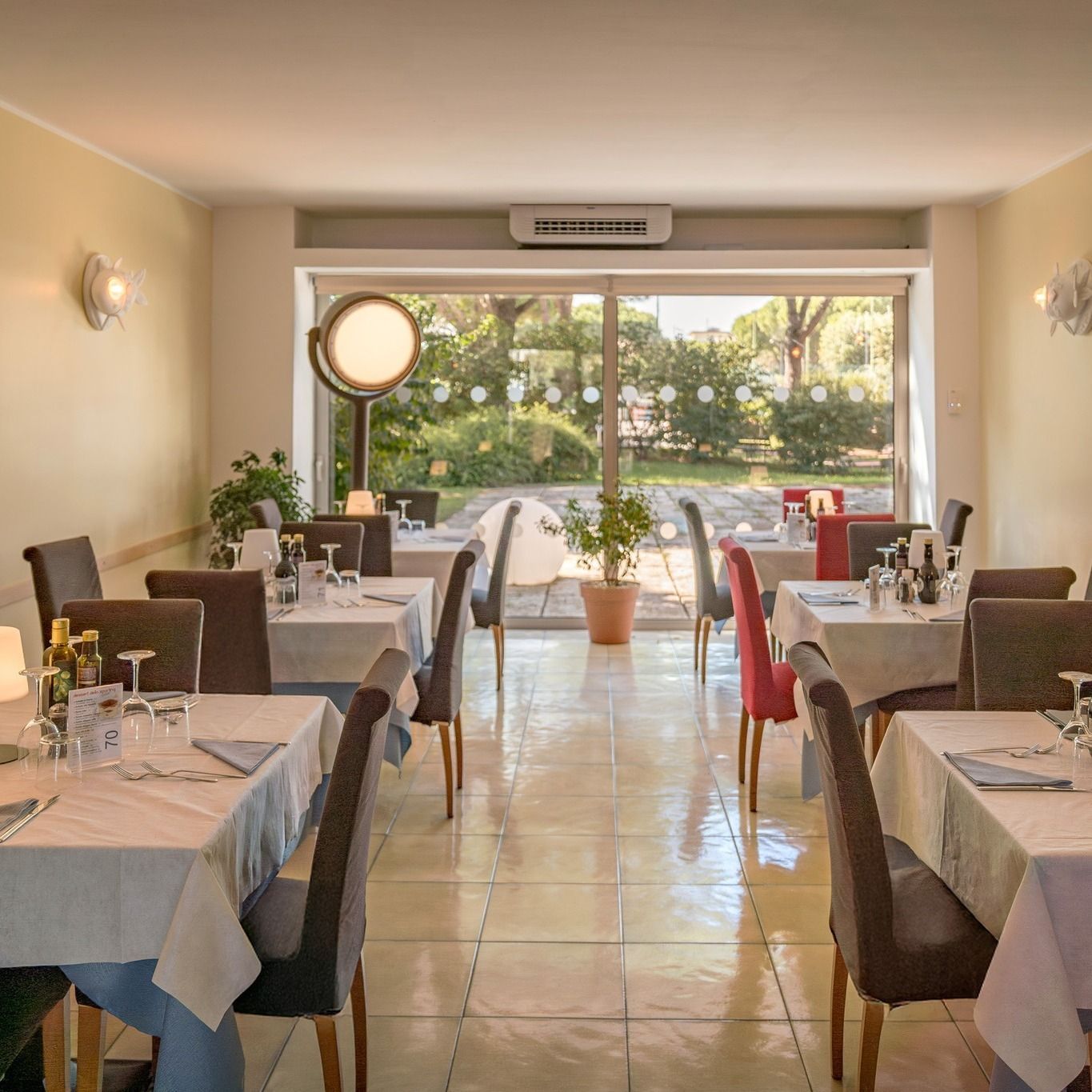Sala da pranzo del ristorante con tavoli apparecchiati per il servizio, con vista sul soleggiato giardino.