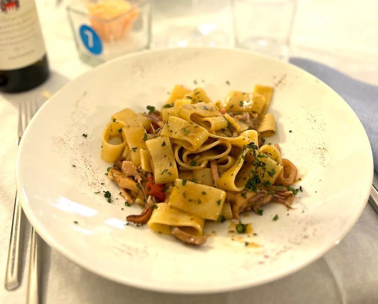 Calamarata, frutti di mare ed erbe aromatiche su un piatto bianco.