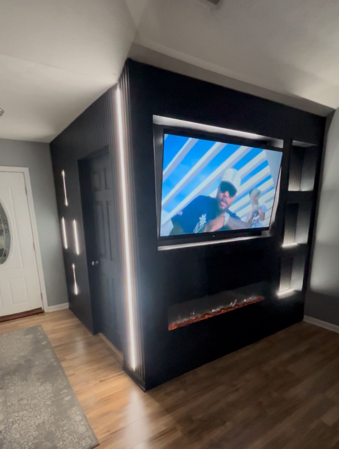 Modern living room with wall-mounted TV, dark accent wall, wood floors, and a round wire coffee table