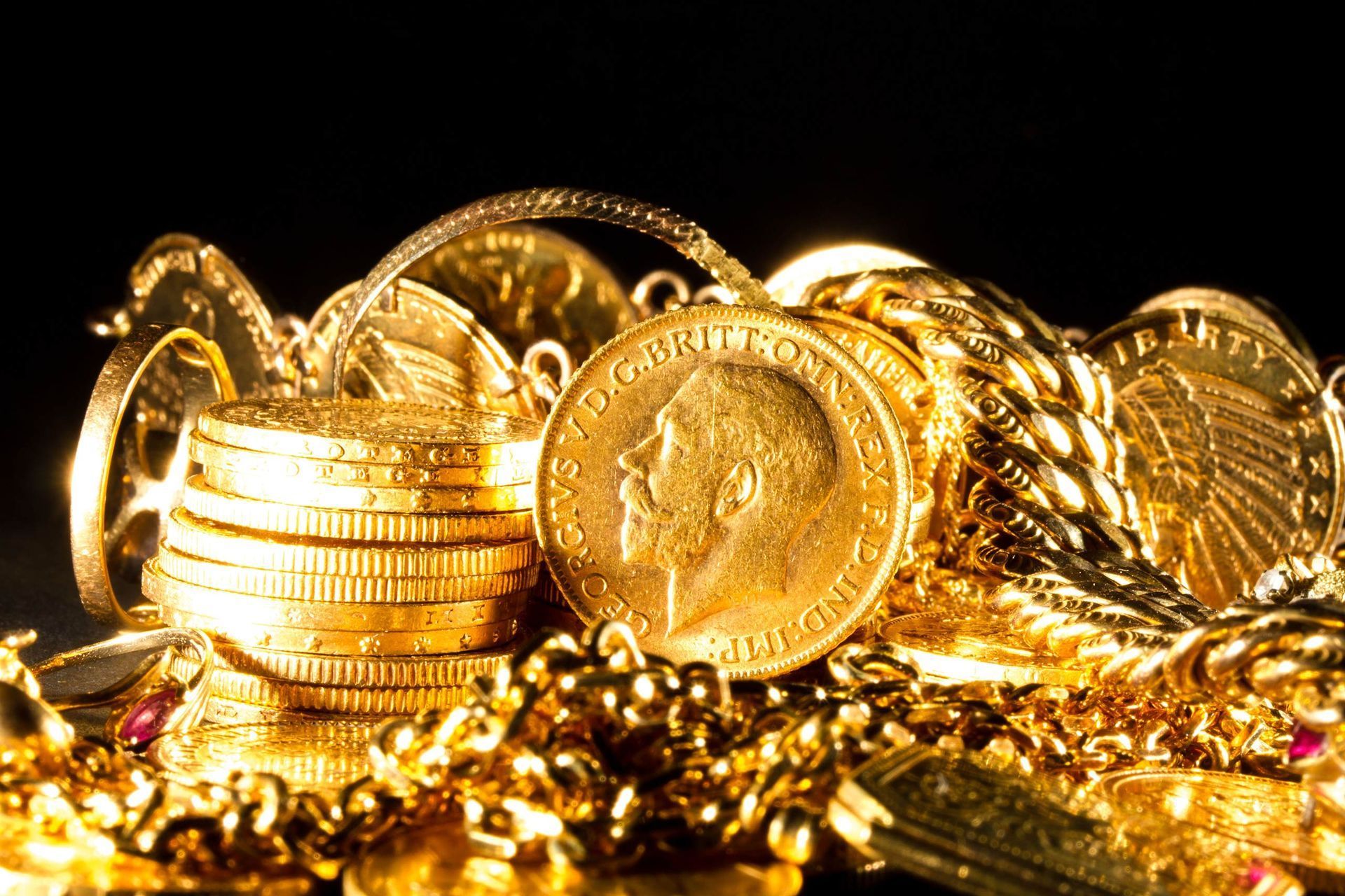 Gold coins and jewelry piled together, glowing on a black background