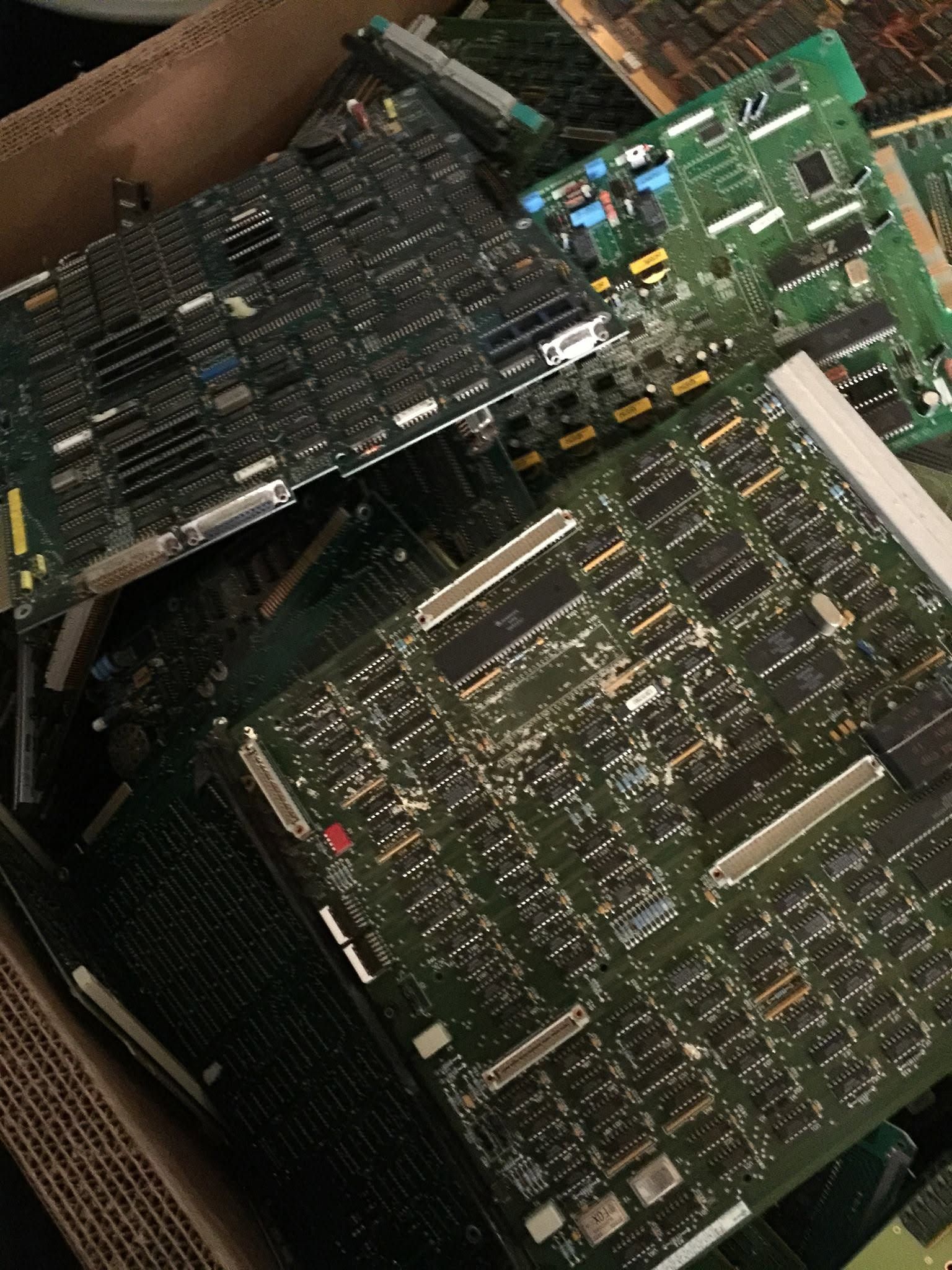 Close-up of stacked circuit boards with dense black and green components in a cardboard box
