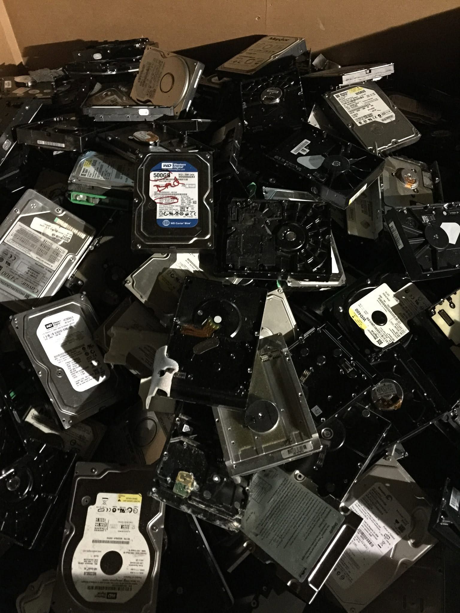 Pile of discarded hard drives and electronic parts in mixed black, silver, and white tones.