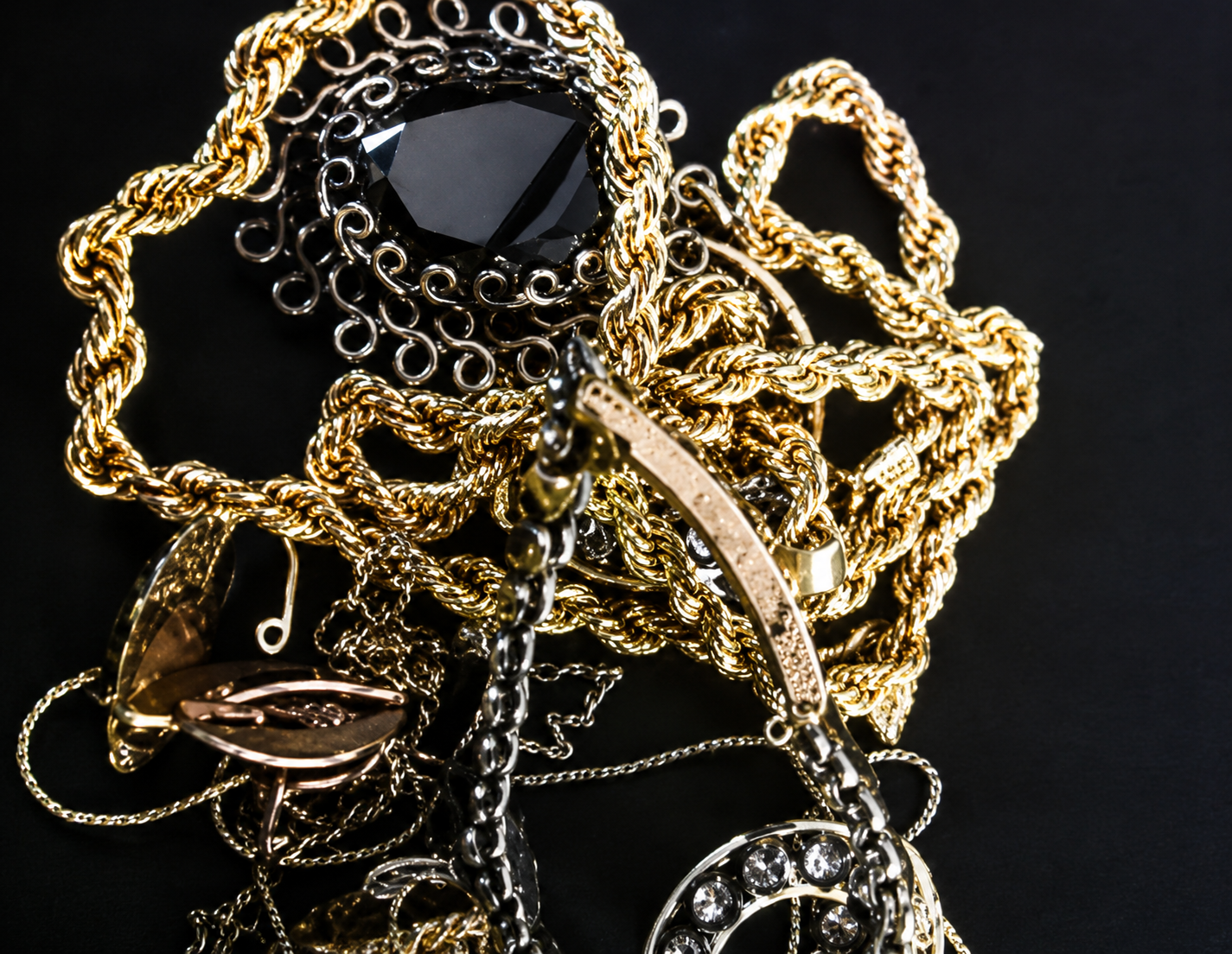 Gold and black tangled necklaces with a large black gemstone pendant on a dark background