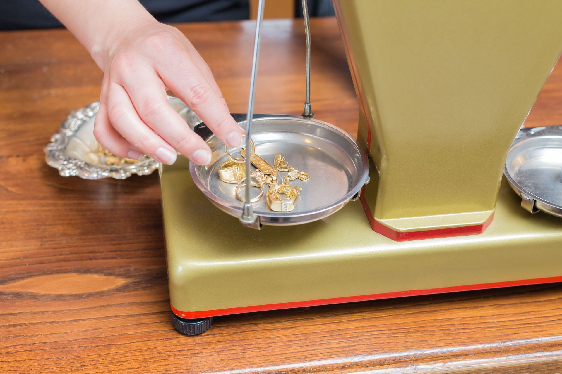 Hand placing small gold pieces into a silver bowl on a tabletop next to a gold base and metal rods