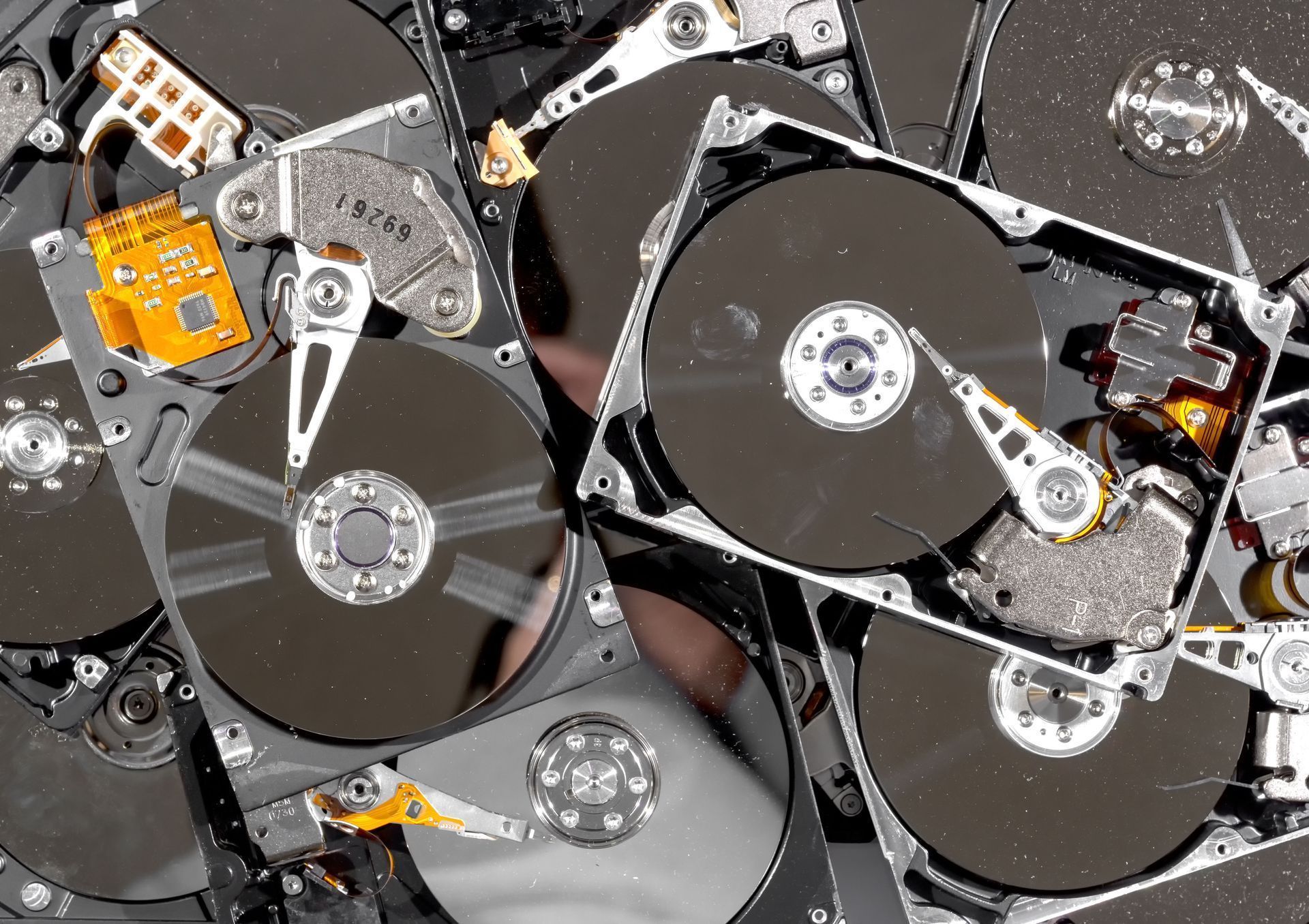 Pile of disassembled hard drive platters and components with silver and black metal parts.