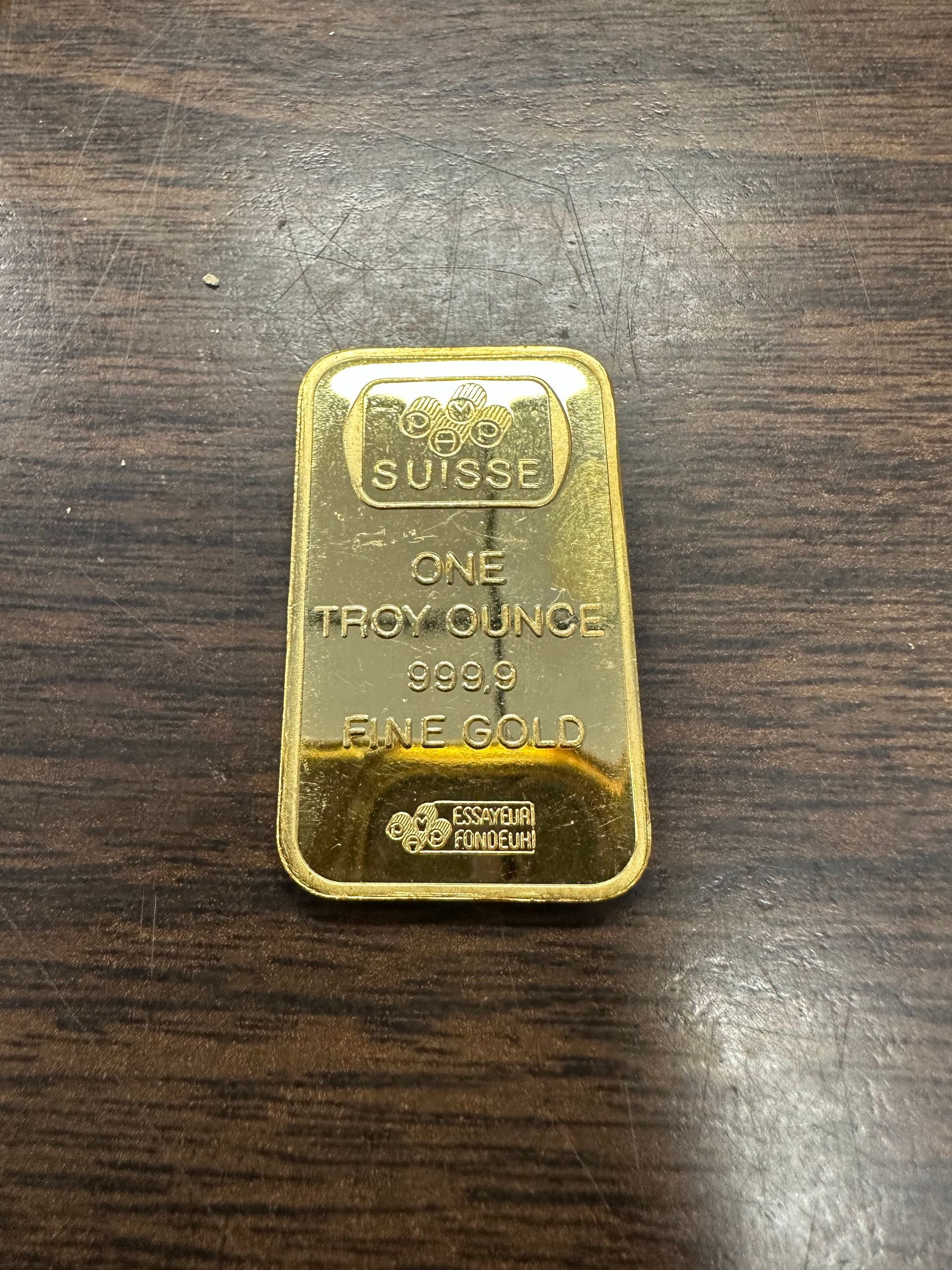 Small gold bar on a dark wooden surface, stamped with text.