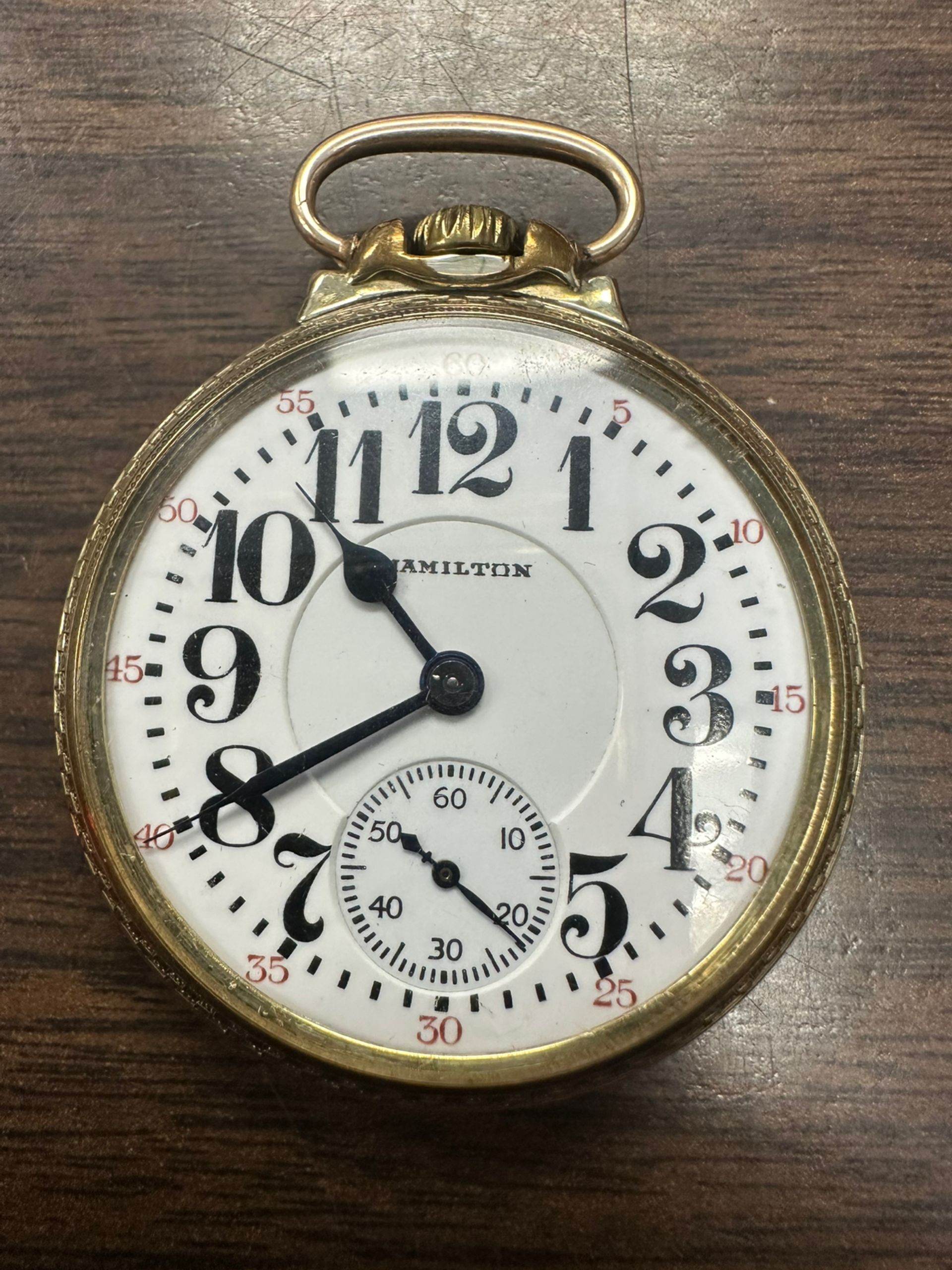 Vintage gold pocket watch with white face and black Roman numerals, showing about 10:40.