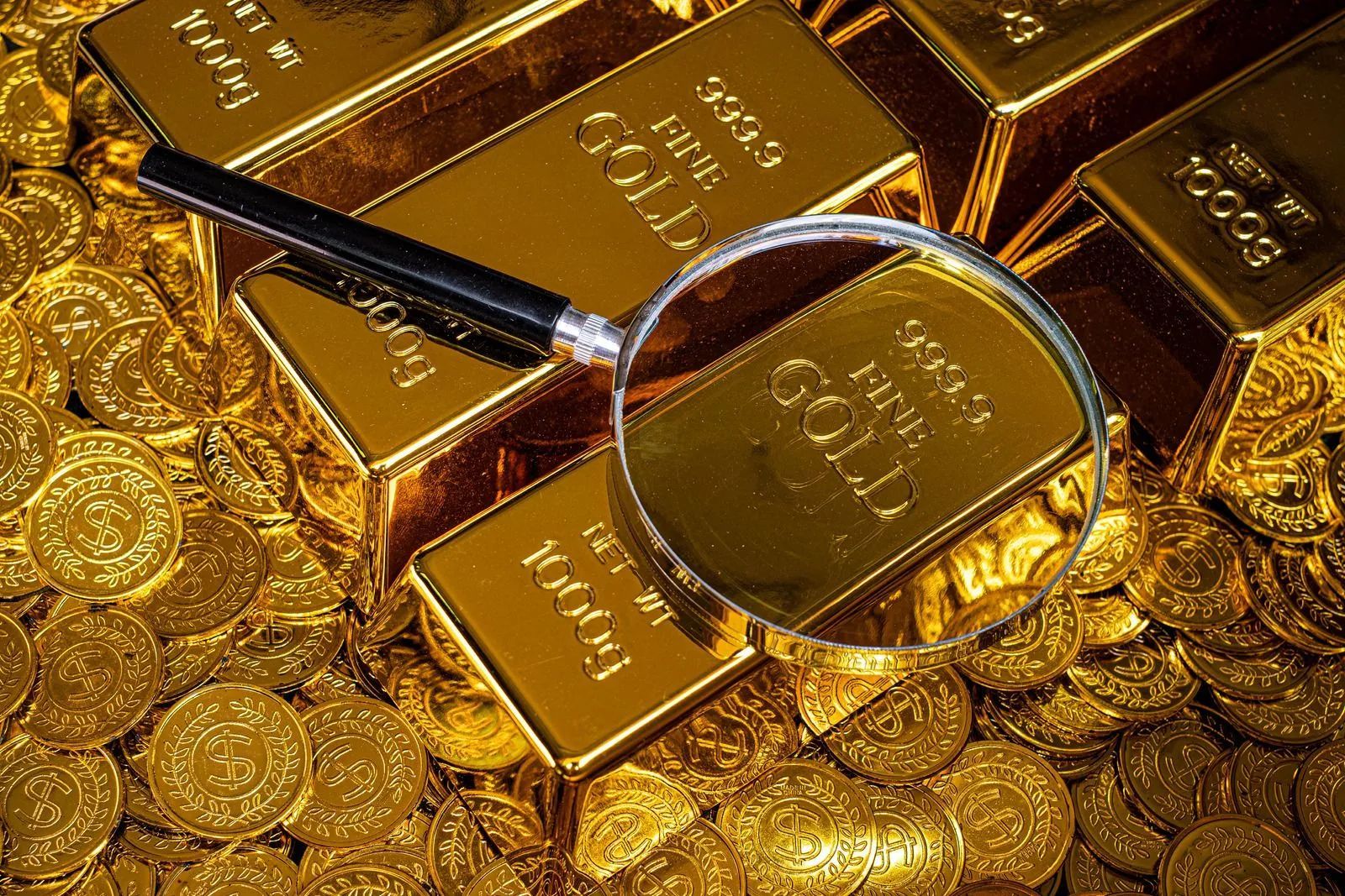 Gold bars and coins under a magnifying glass, showing detailed gold texture and shine.