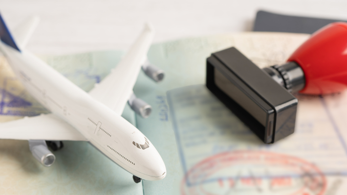 A toy airplane sits on an open passport page next to a red ink stamp, symbolizing international travel.