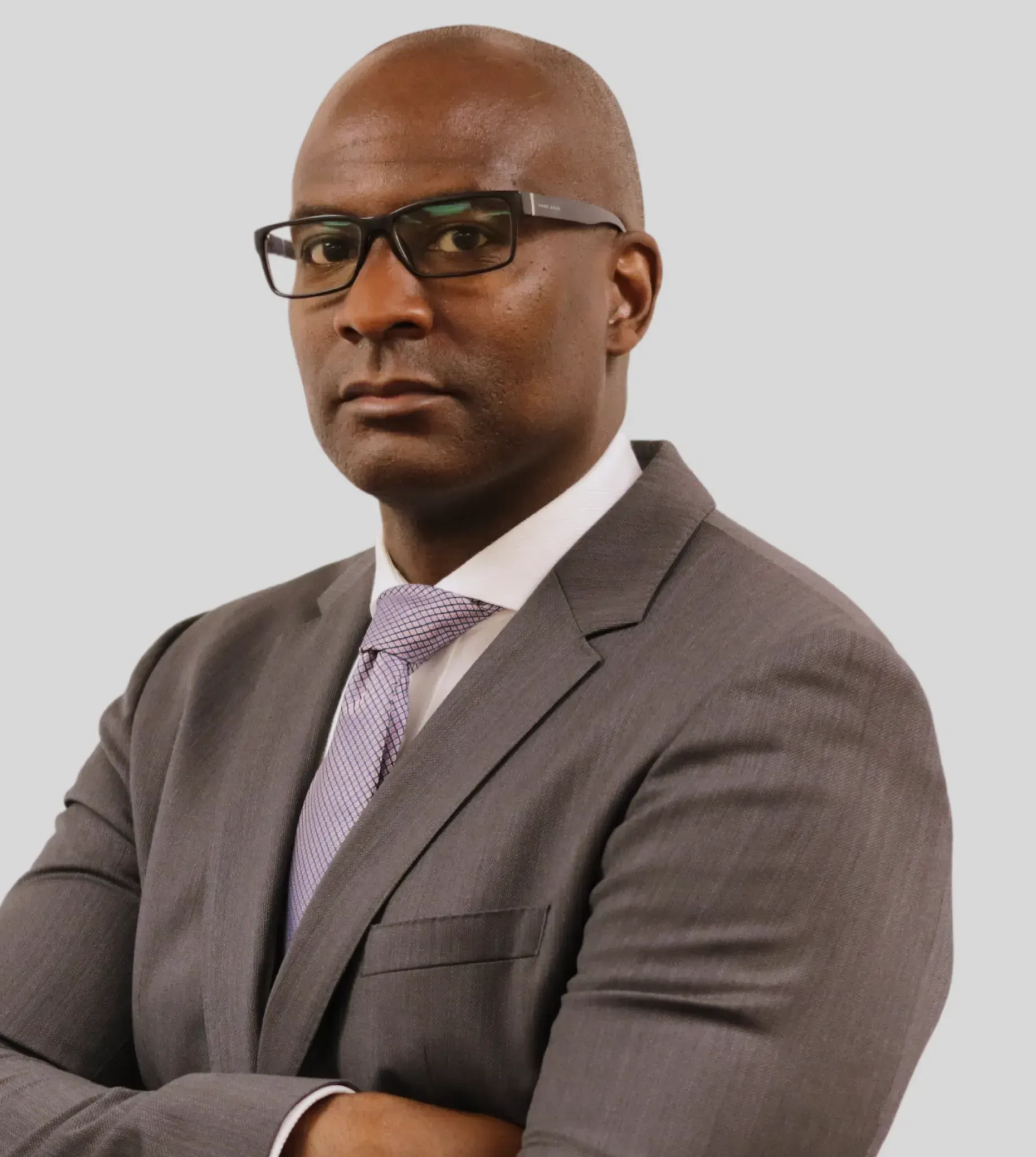 A professional headshot of a person in a gray suit and patterned tie, wearing glasses and standing with arms crossed.