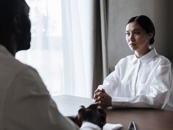 Two people sit across from each other at a desk in a professional, brightly lit room, engaged in a focused conversation.