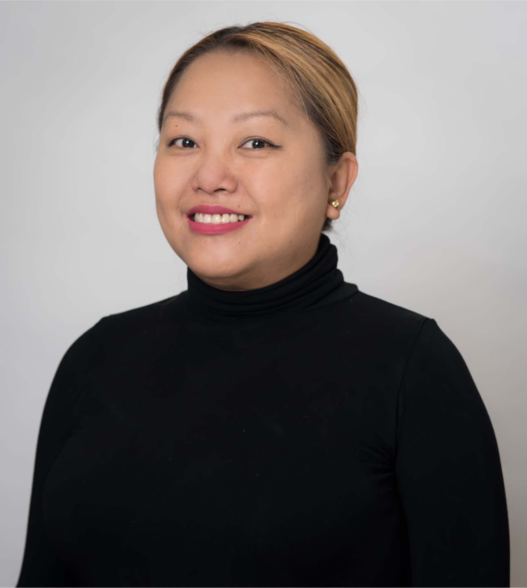 A smiling person with light brown hair pulled back, wearing a black turtleneck against a plain, light gray background.