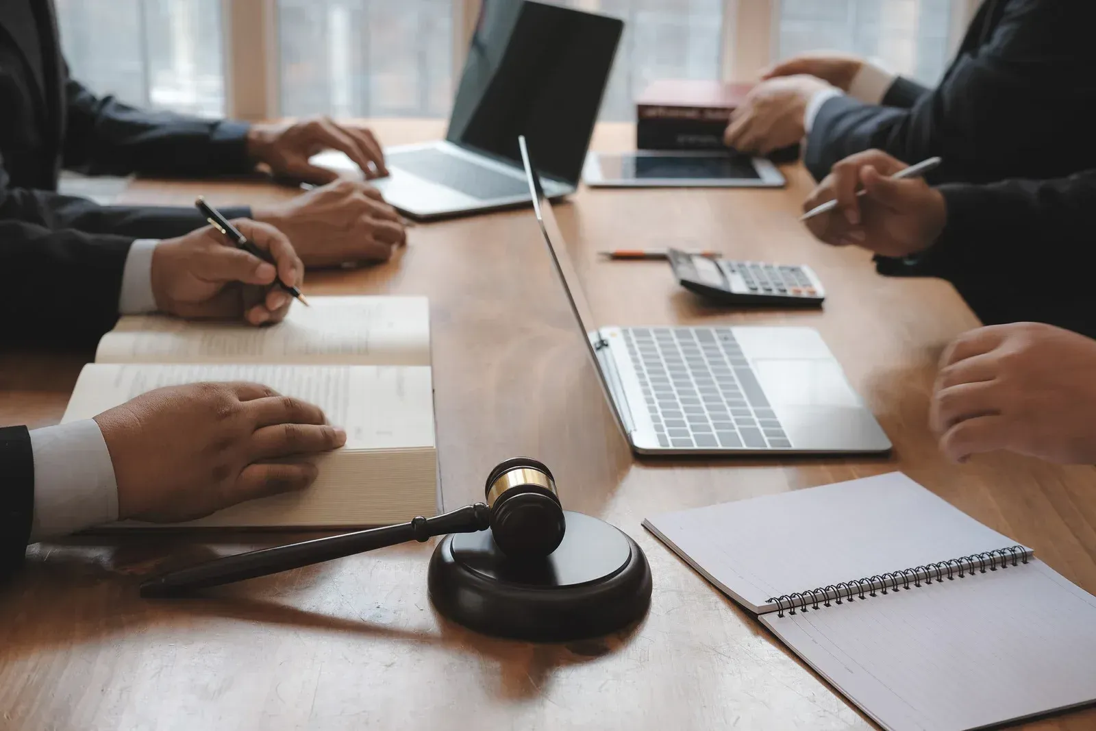People in a meeting table taking notes beside a gavel and laptop