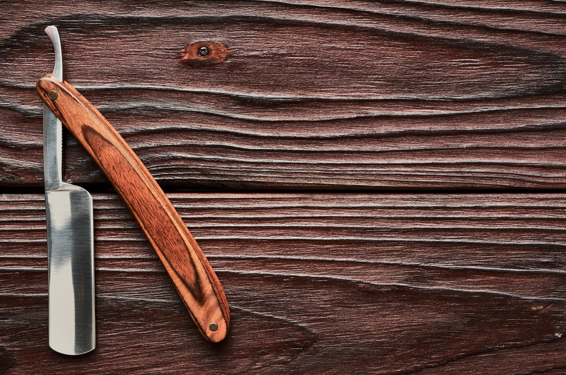 A razor with a wooden handle is sitting on a wooden table.