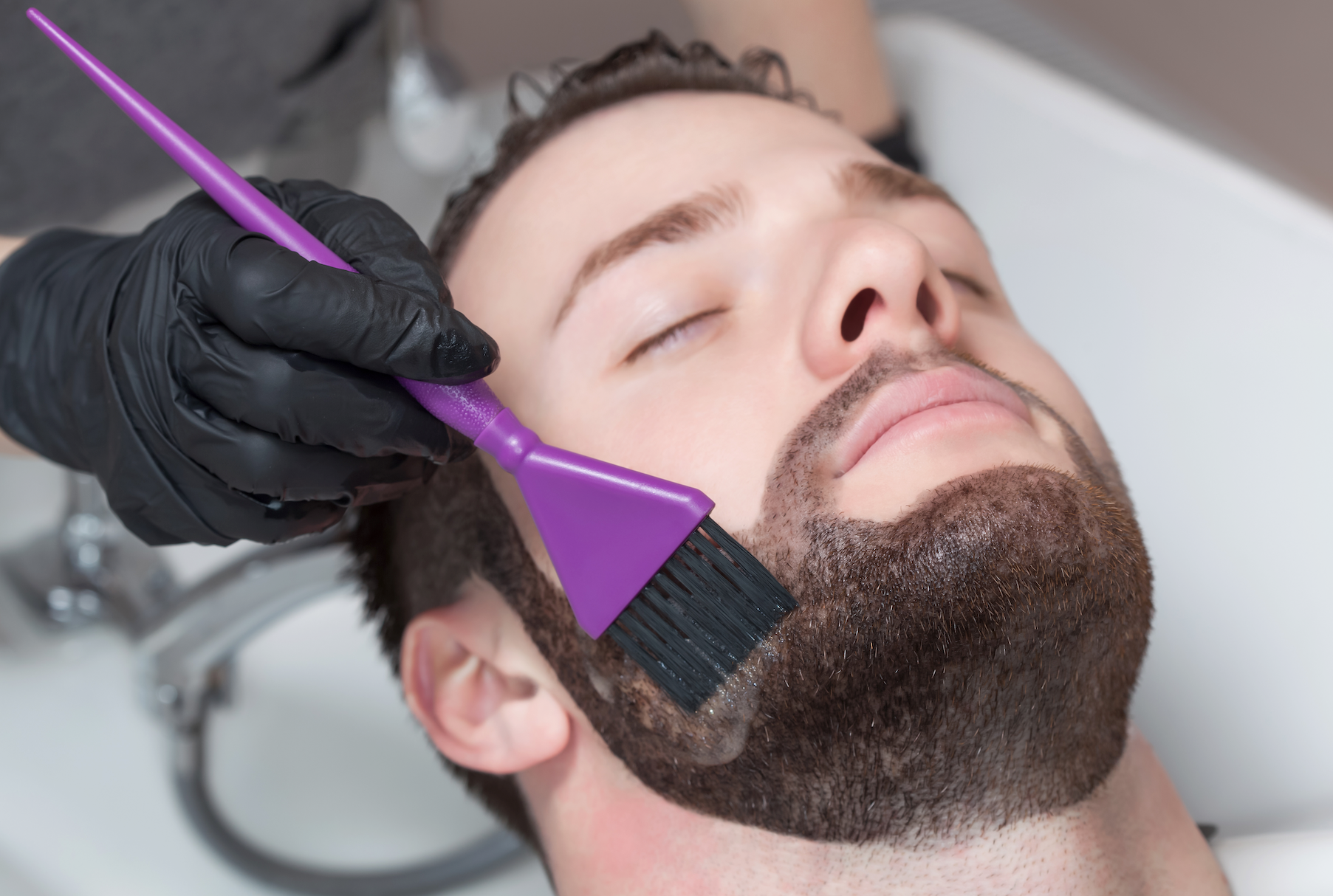 A man is getting his beard dyed in a salon.