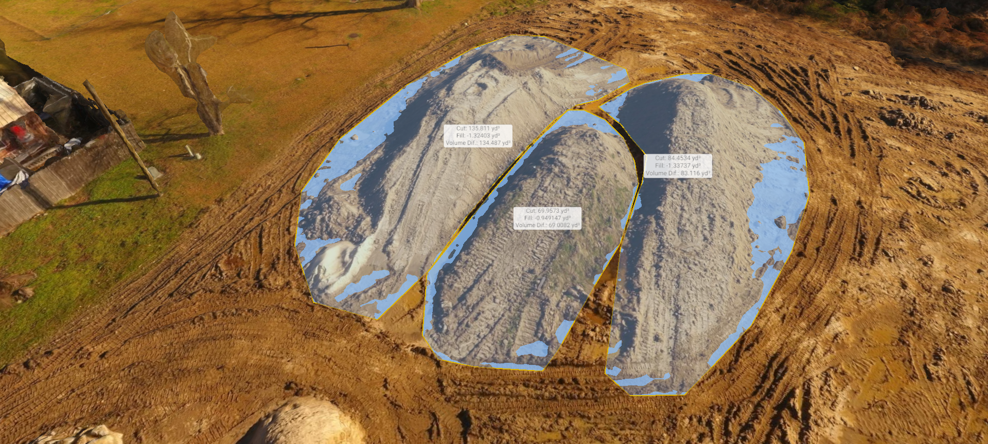 Aerial view of a blue-tarped mound or structure on a dirt site with labeled sections and nearby machinery