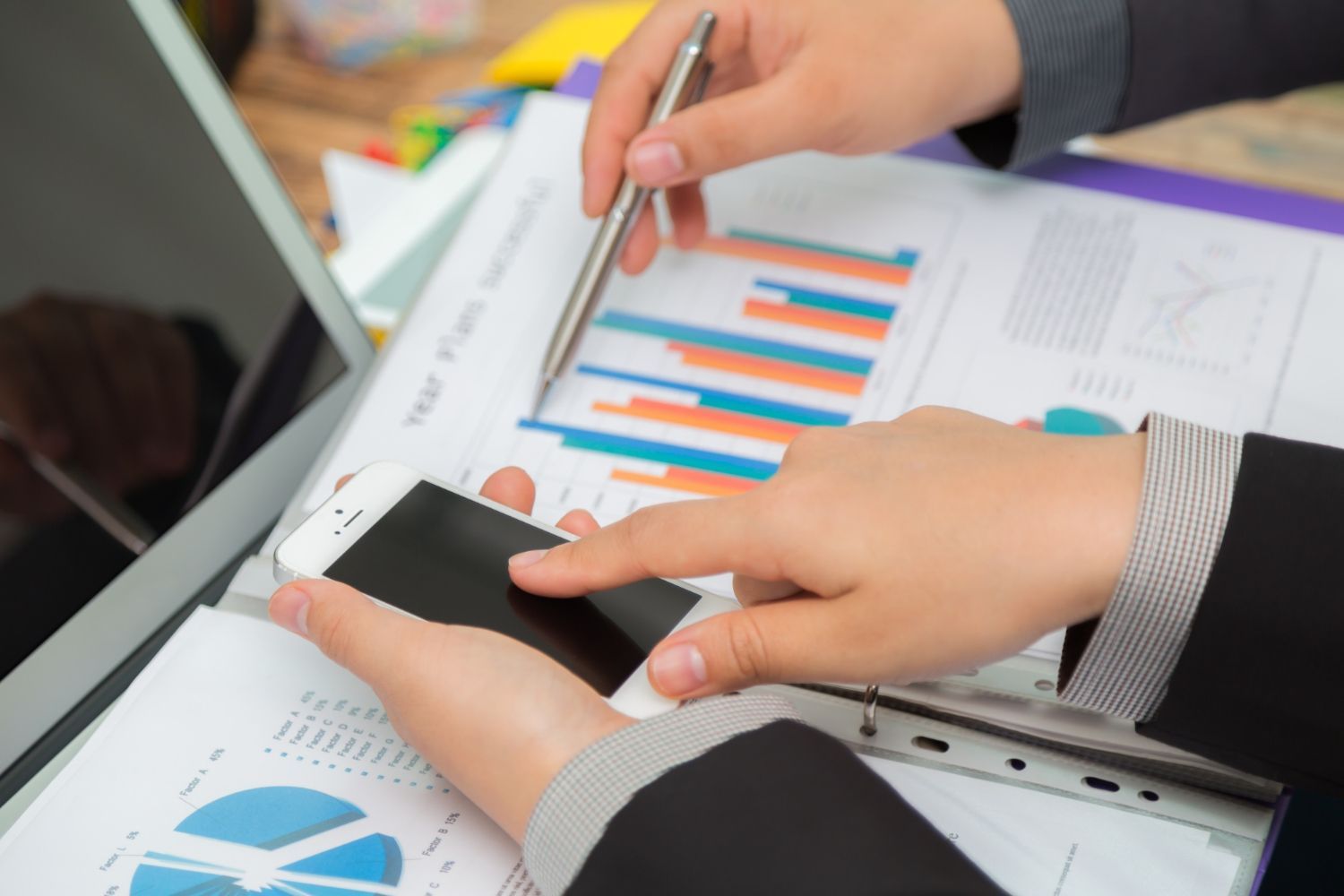 Two professionals in business suits analyze financial charts on paper and a smartphone.