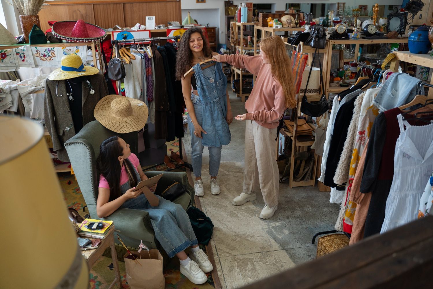 Three people in a cluttered clothing store, with one person seated and two others looking at a denim garment.