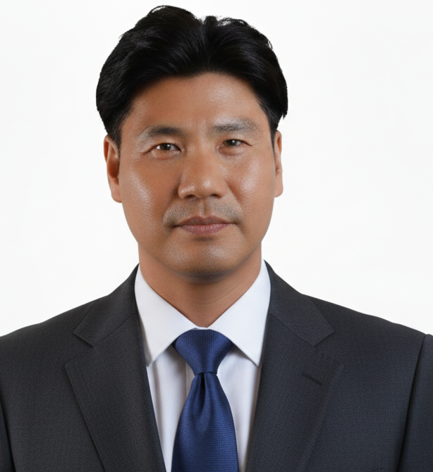 Headshot of a person with dark hair wearing a suit and blue tie against a plain white background.