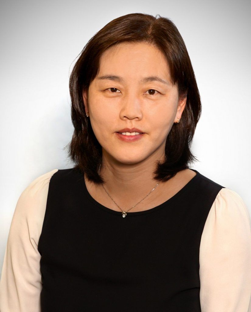 A professional headshot of a person with shoulder-length dark hair, wearing a black top with white sleeves.