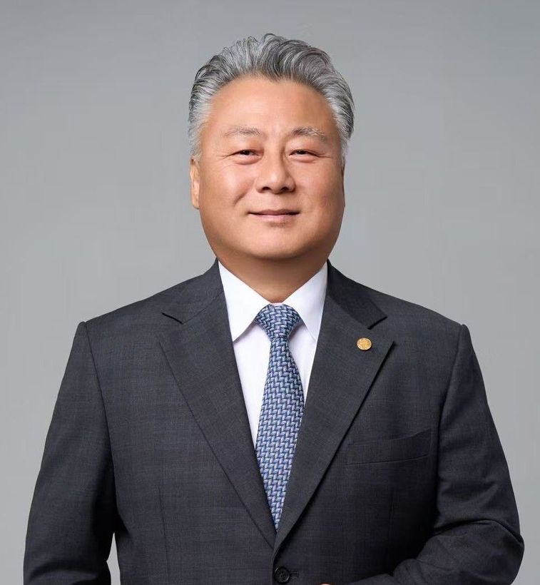 A professional portrait of a man wearing glasses, a navy blue suit, a patterned tie, and a white pocket square.