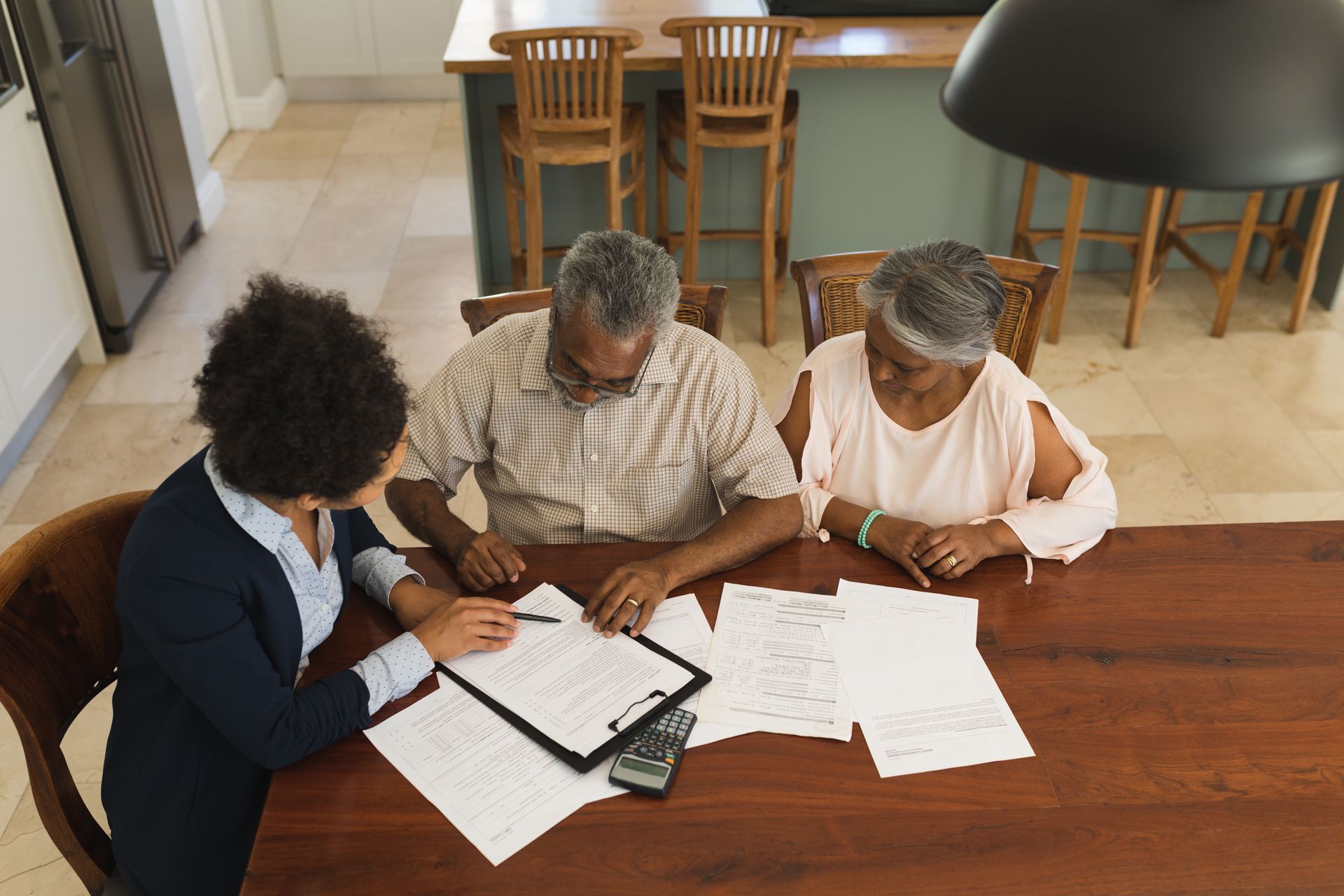 A professional works with a couple at a table, reviewing financial documents and paperwork in a home setting.