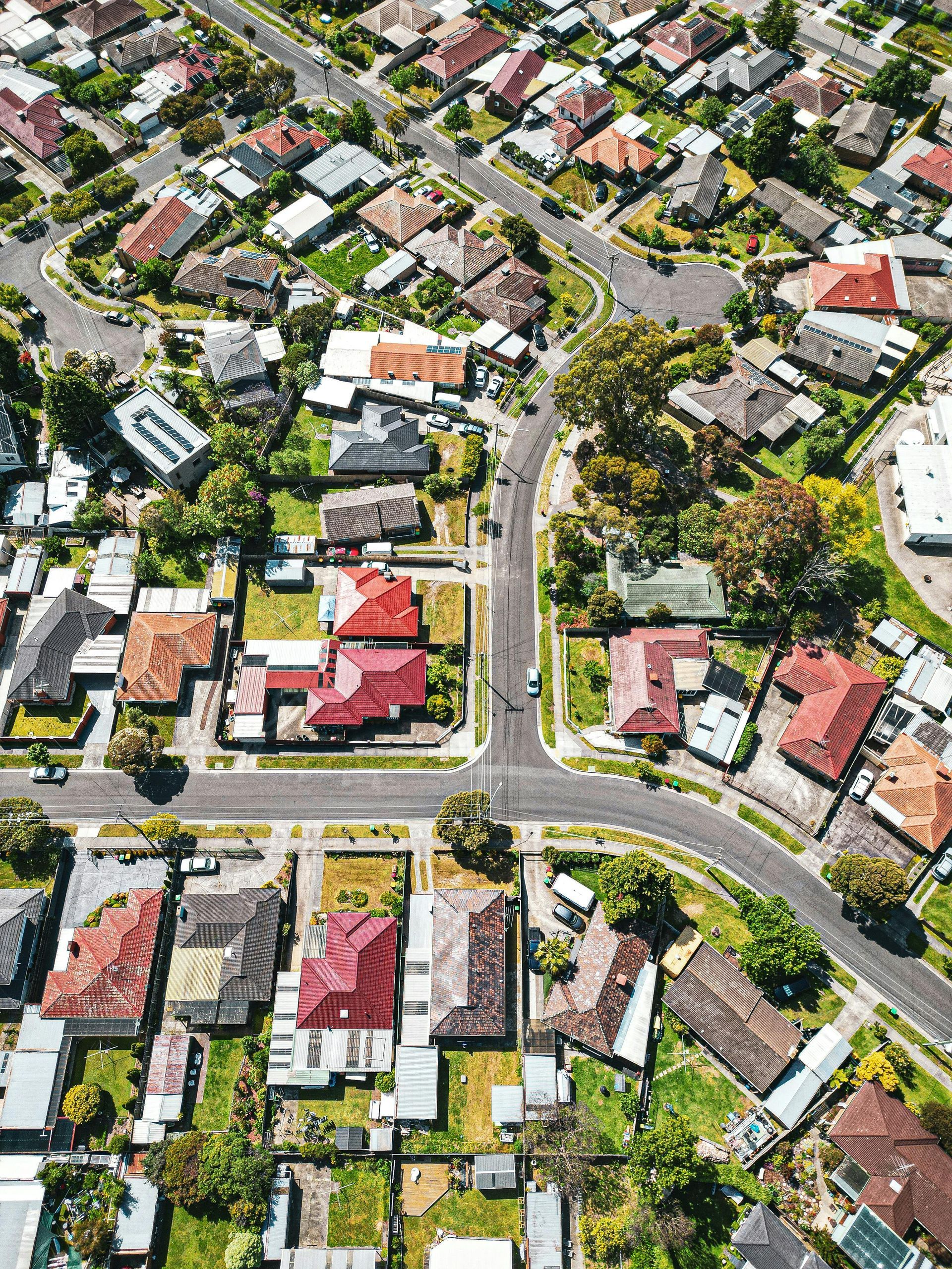 Aerial view of a residential neighborhood with houses featuring various roof colors surrounded by green trees and streets.