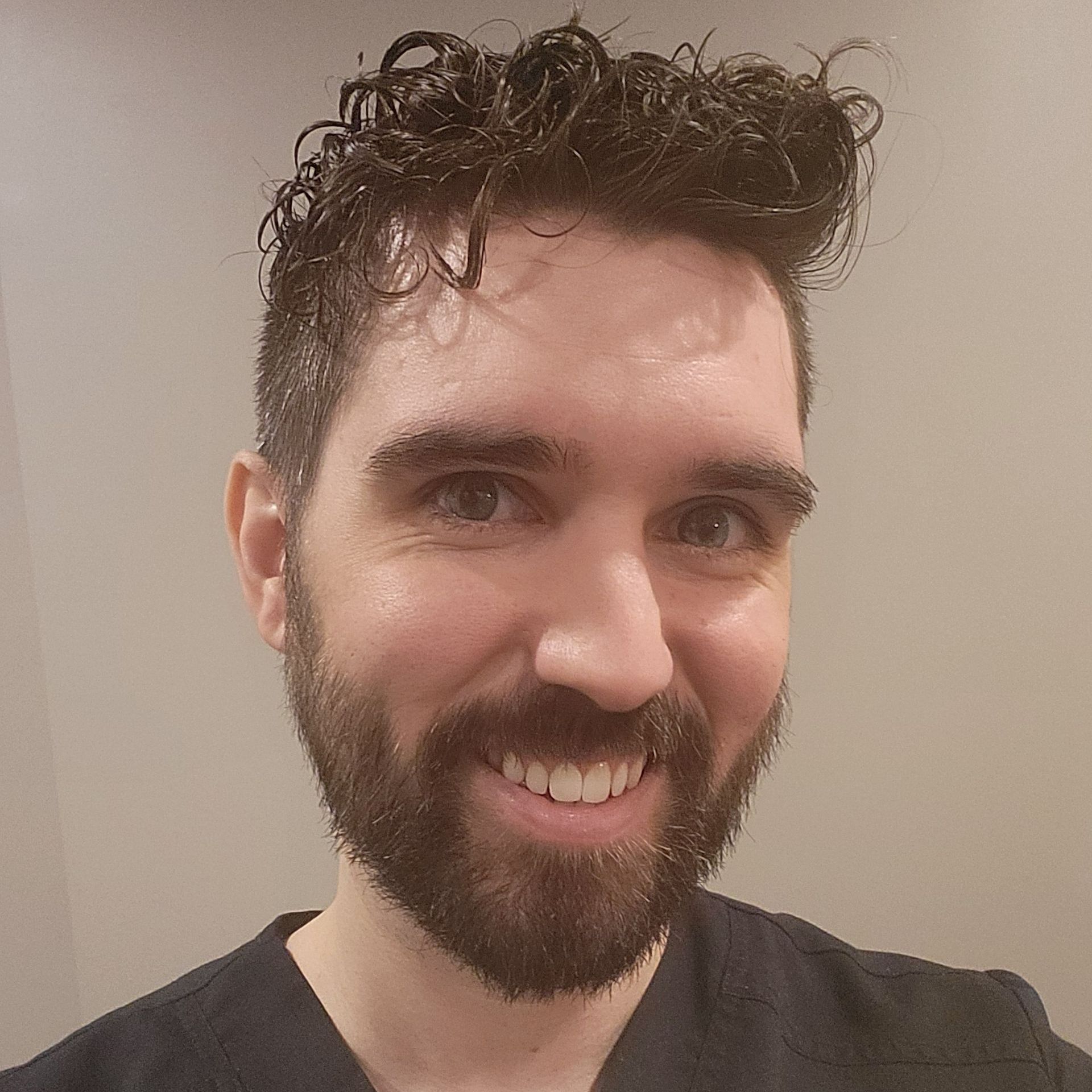 A man with a beard and curly hair is smiling for the camera.