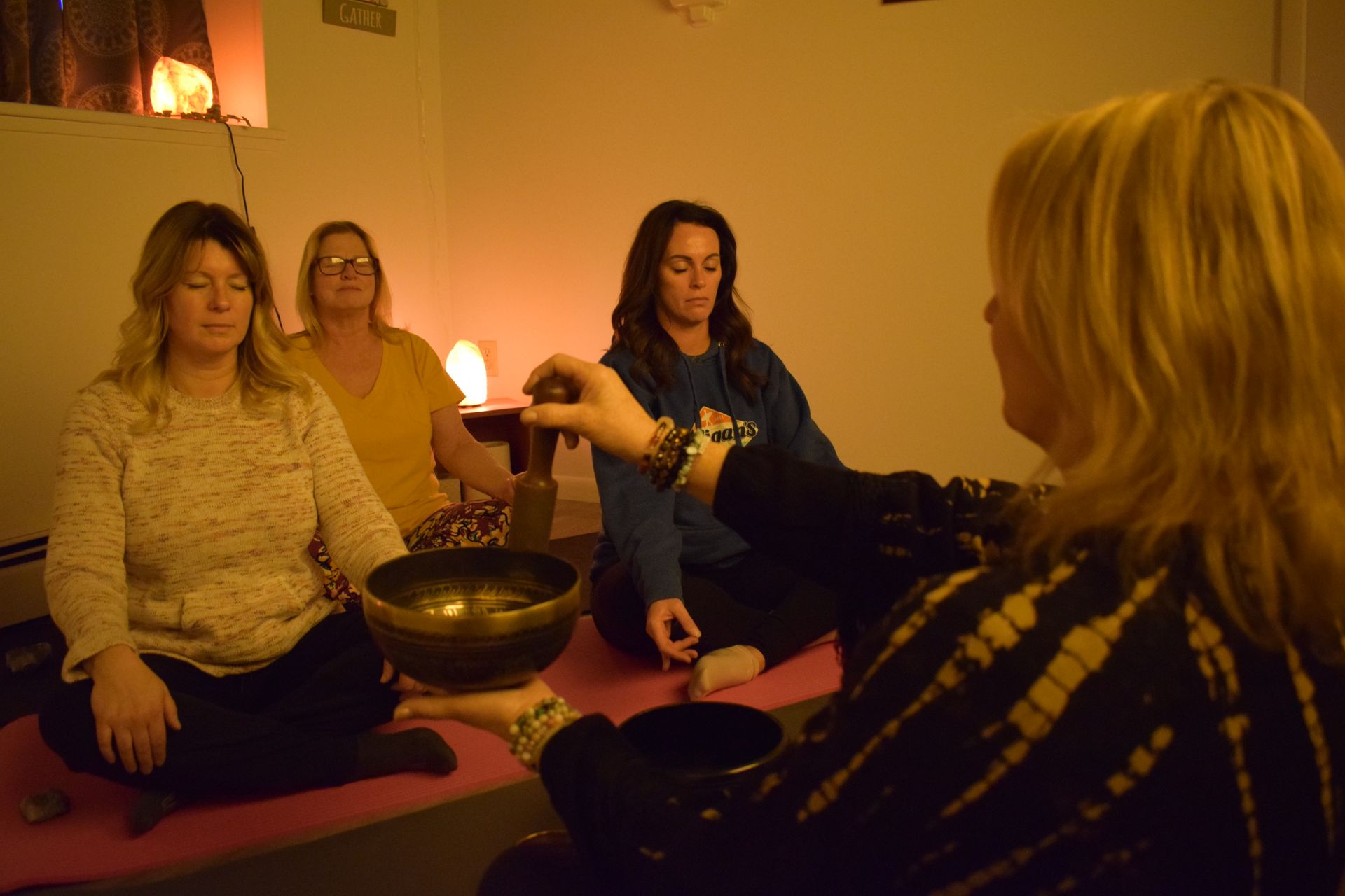 A group of women are sitting on a yoga mat in a dark room.