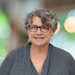 A woman wearing glasses and earrings is smiling for the camera.